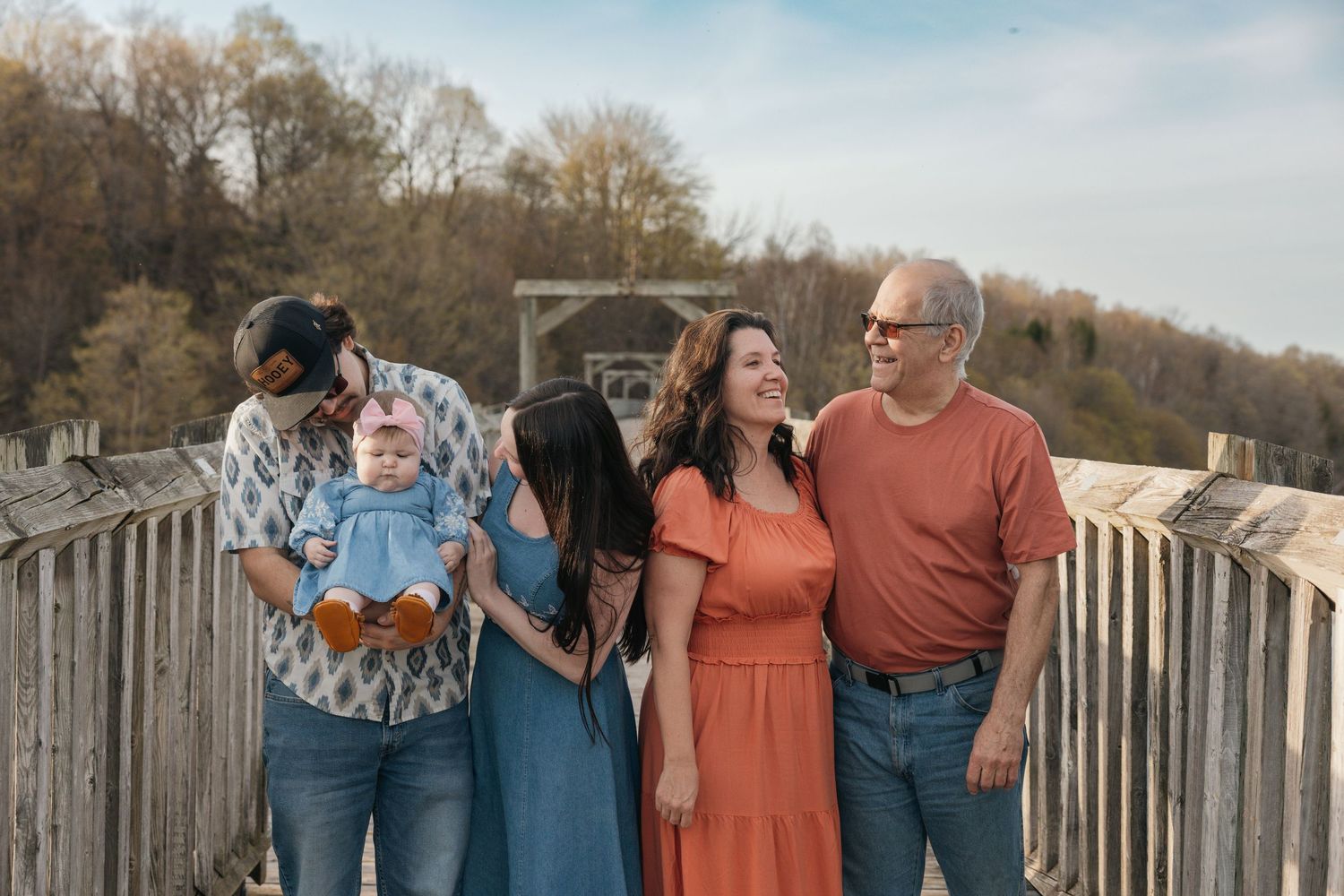 Extended family group laughing together on a wooden bridge during an outdoor photo session.