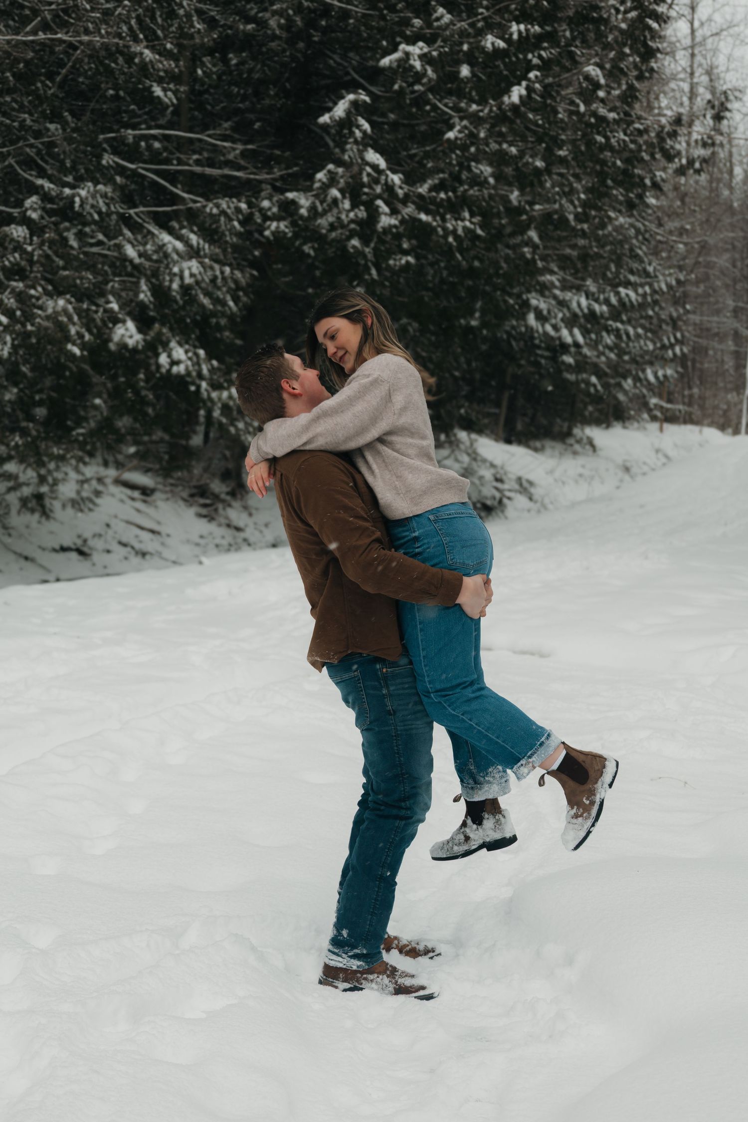 Man lifting woman in his arms while laughing in a snowy forest setting.
