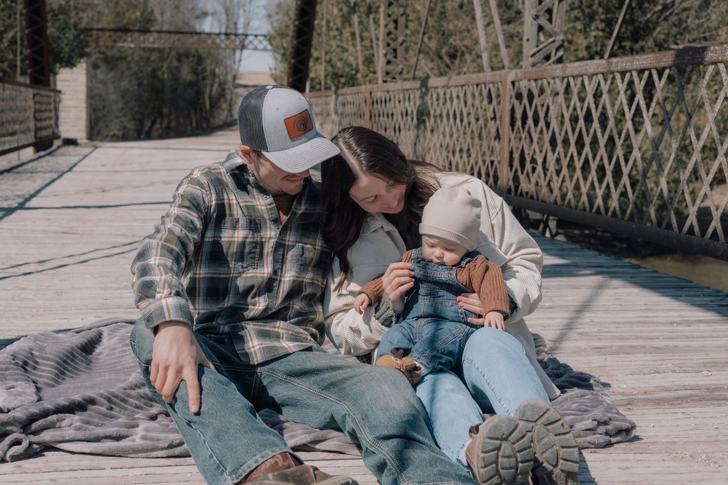 Family sitting together on a wooden bridge enjoying a sunny outdoor moment.