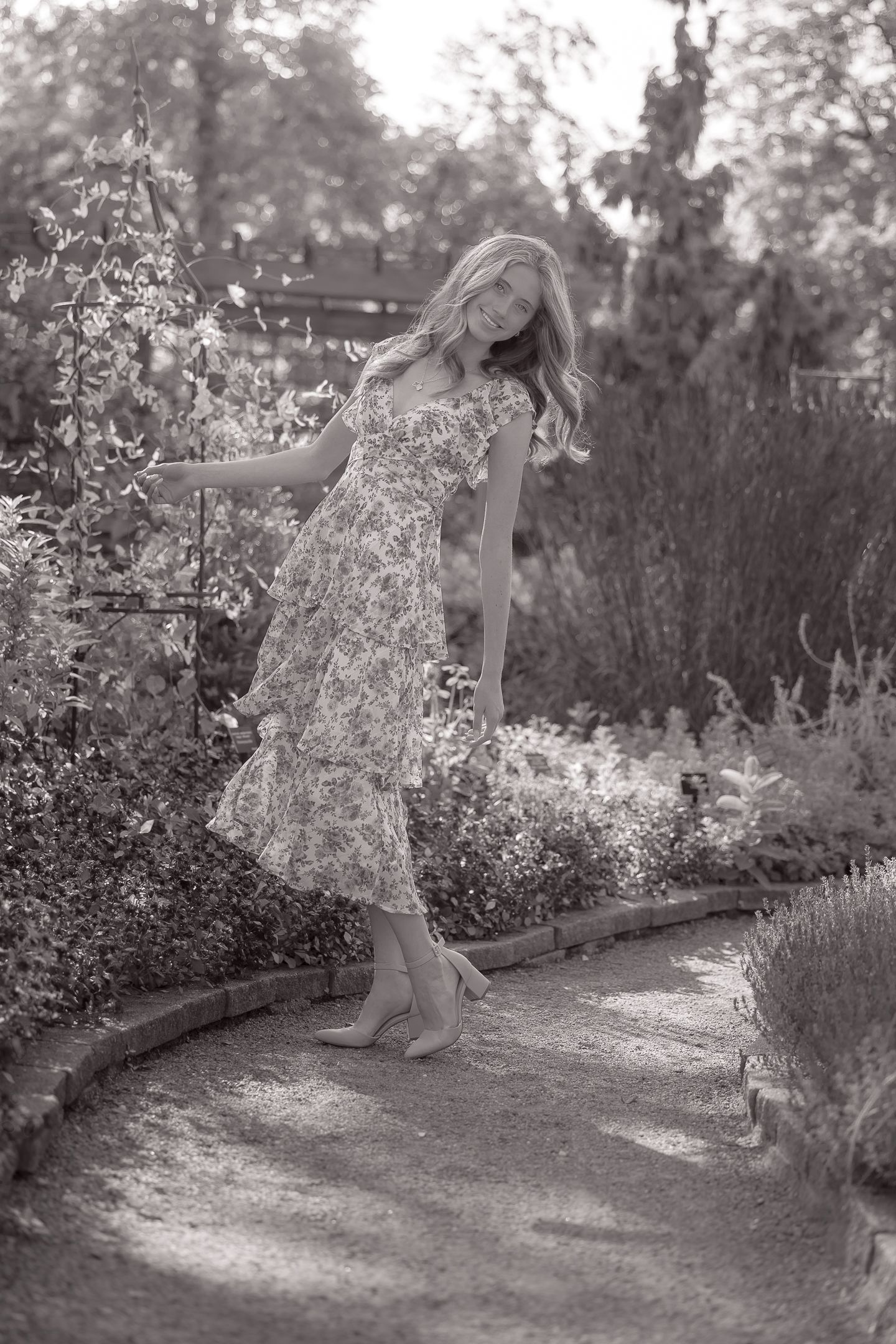 Child playing and twirling in a garden path surrounded by blooming flowers.