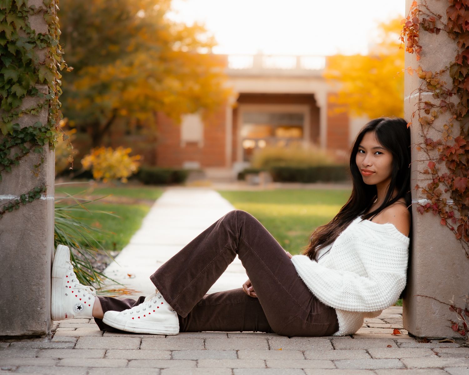 Person in casual attire lying on stone path during sunset with autumn colors.