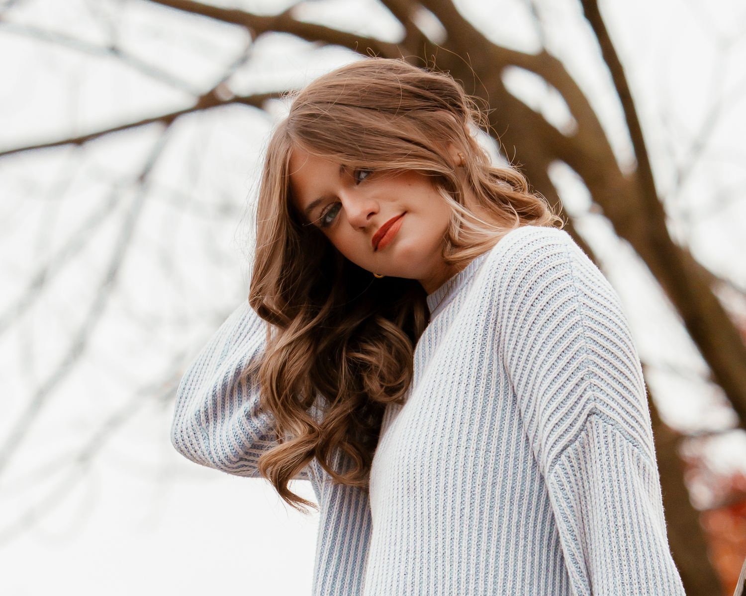Woman in gray knit sweater posing against white winter background.