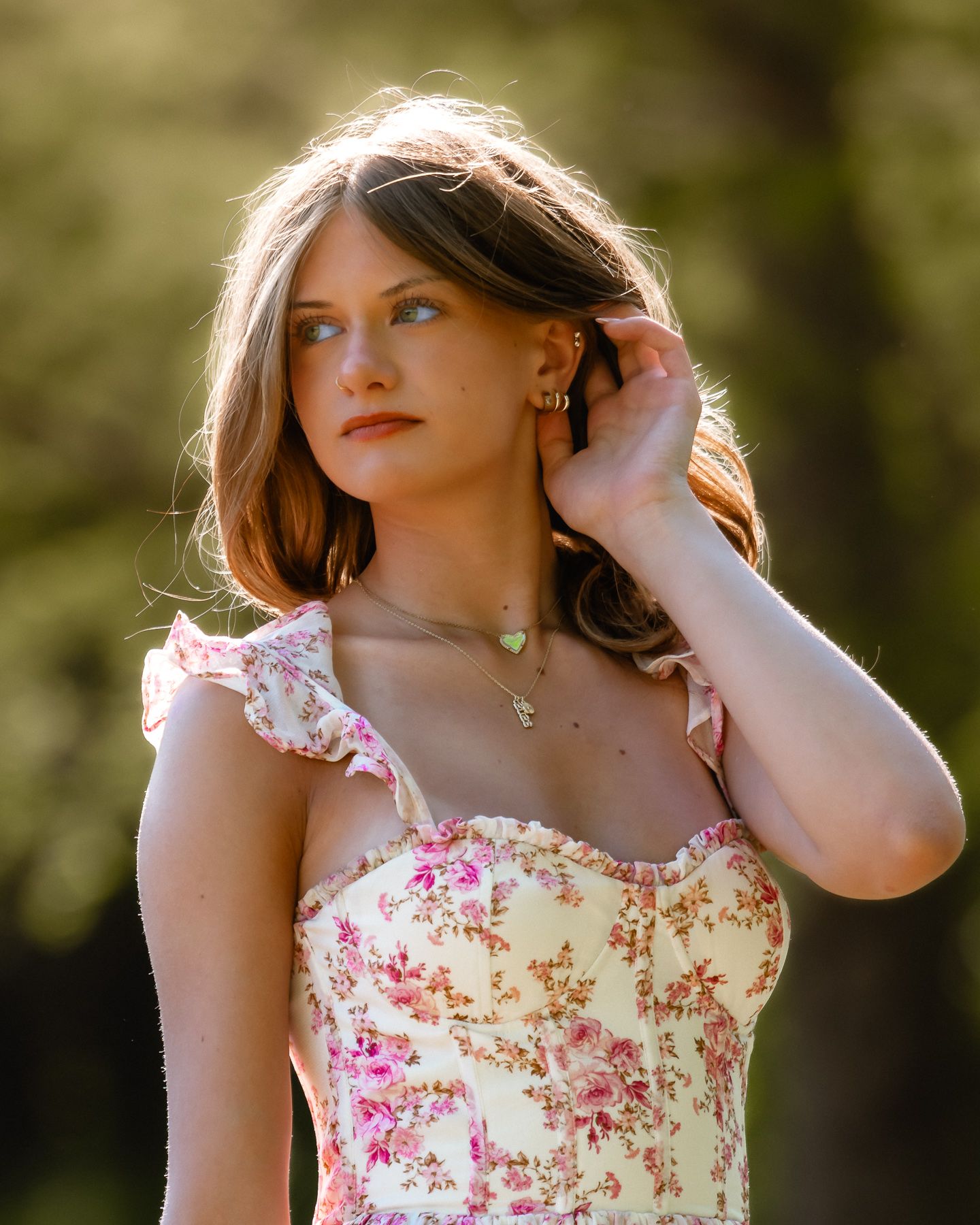Young woman in floral sundress with ruffled shoulders, wearing gold jewelry, posing outdoors in soft natural light.