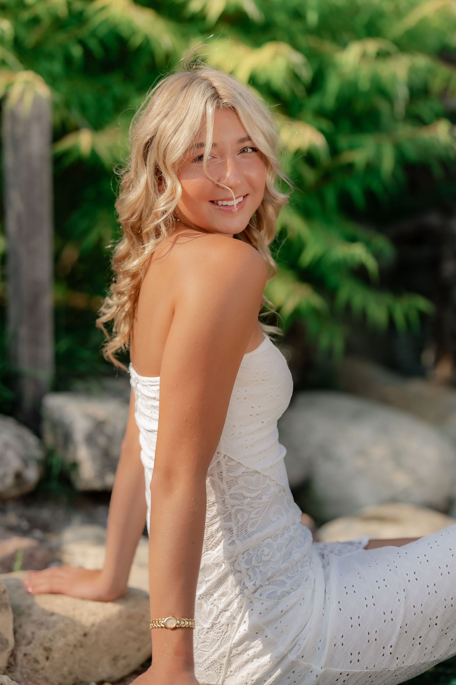 A person in a white eyelet lace dress poses outdoors against a natural green foliage background.