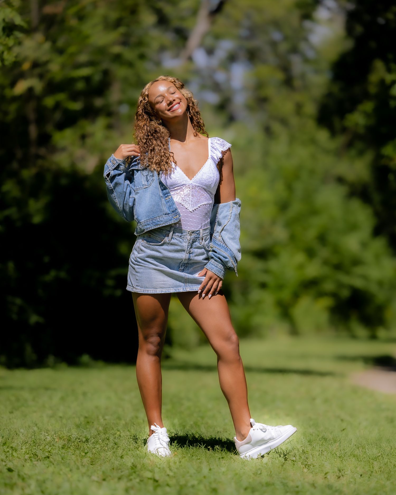 Casual summer photoshoot with denim jacket and white sneakers on green grass.