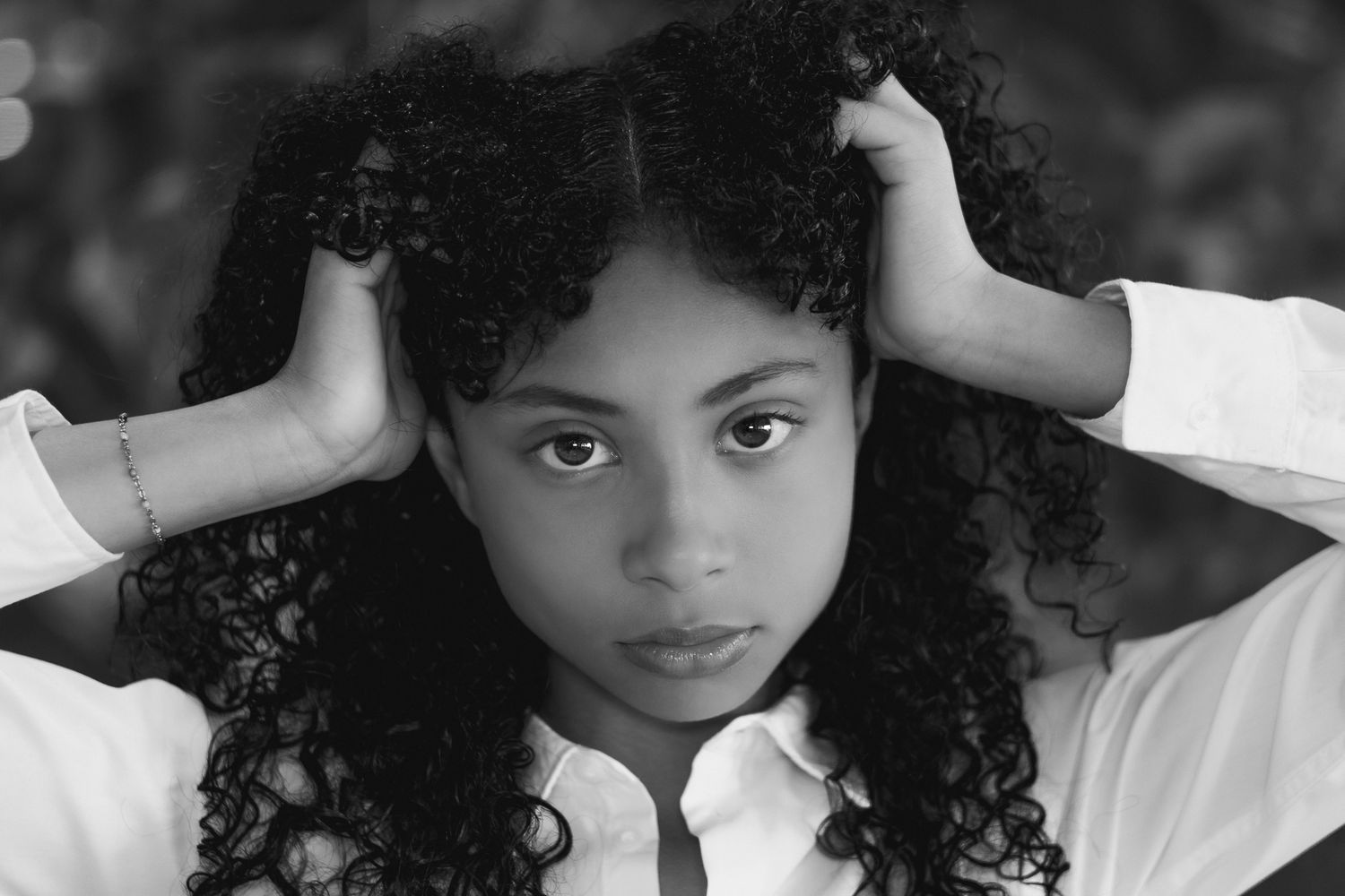 Black and white portrait of a woman with natural curly hair in white shirt.