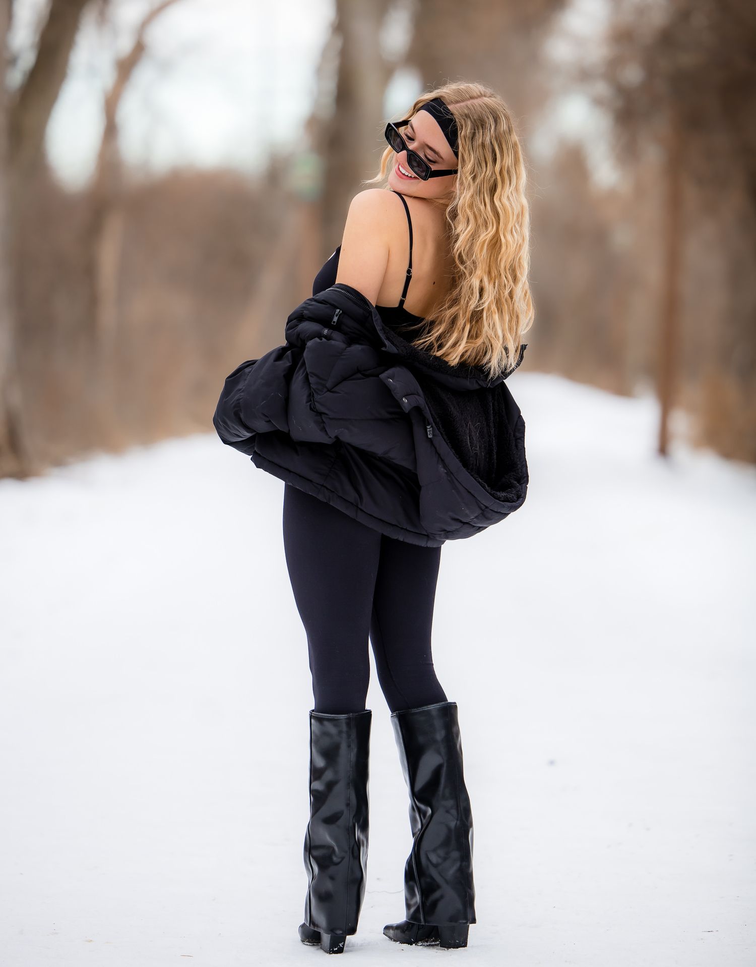 A person in a black winter outfit poses against a snowy landscape background.