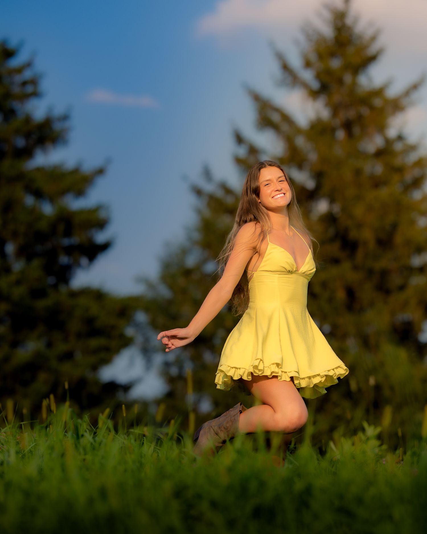 Dancing and twirling in a yellow ruffled dress on a grassy hillside at sunset.