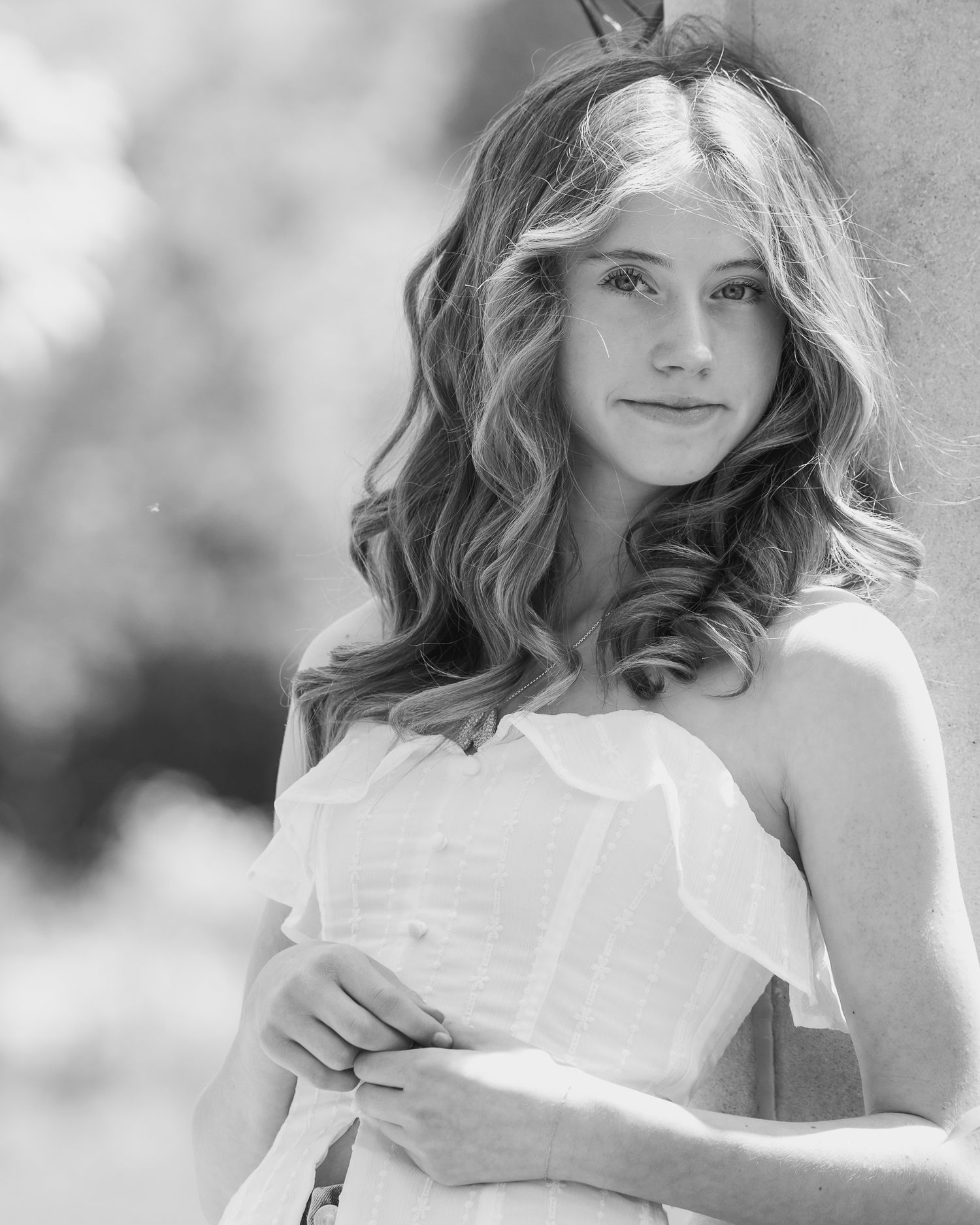 Artistic black and white portrait of a woman in white dress with wavy hair and natural lighting.