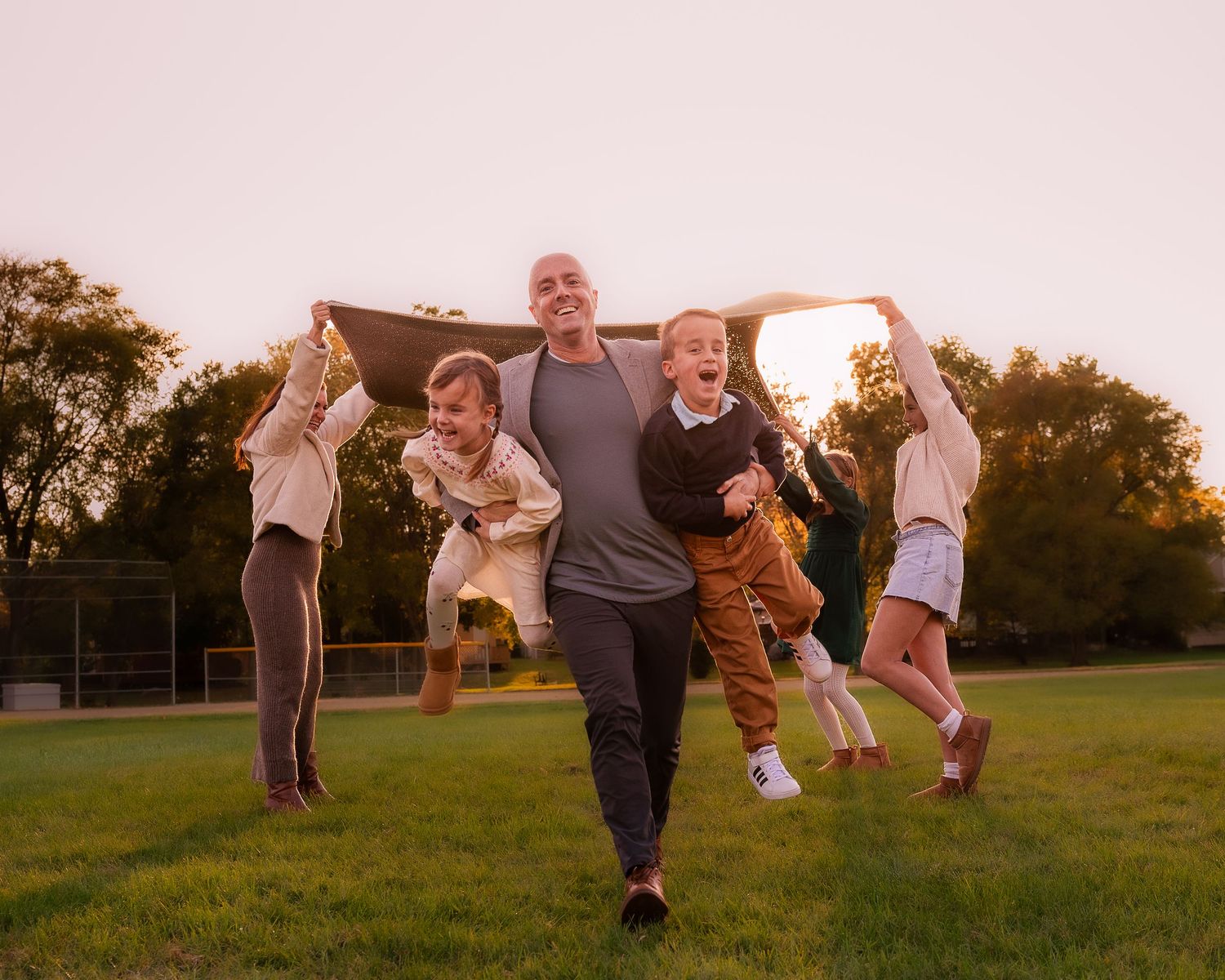 Family members jumping and playing together in a grassy field during golden hour sunset.