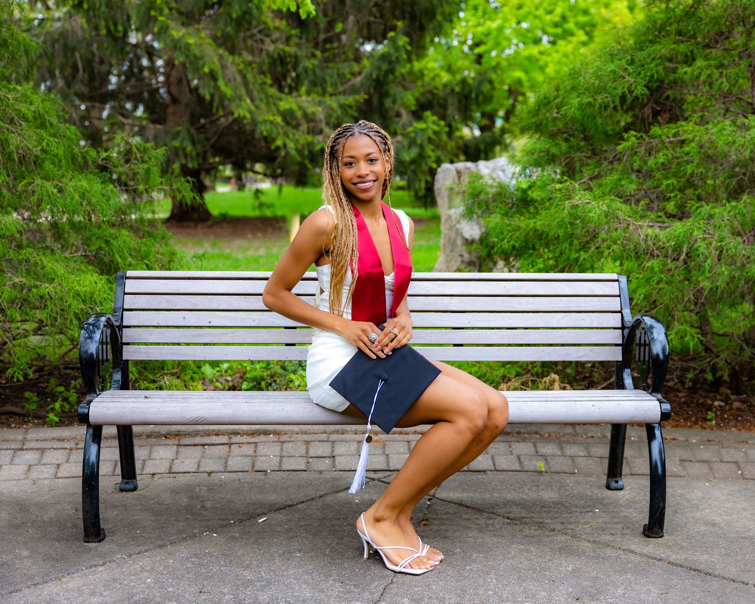 Graduate poses on park bench in various casual positions wearing academic regalia.