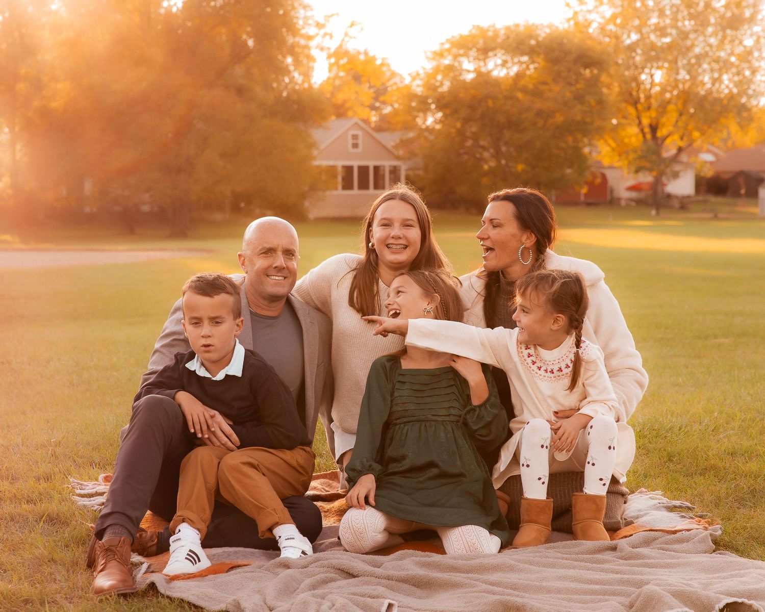 Family relaxing on picnic blanket during golden hour sunset in park.