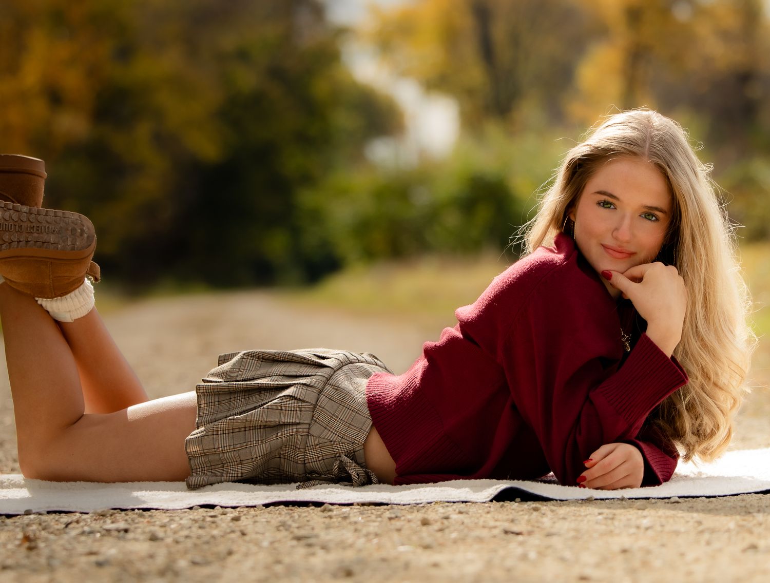Person lying on ground in burgundy sweater during golden hour photography session.