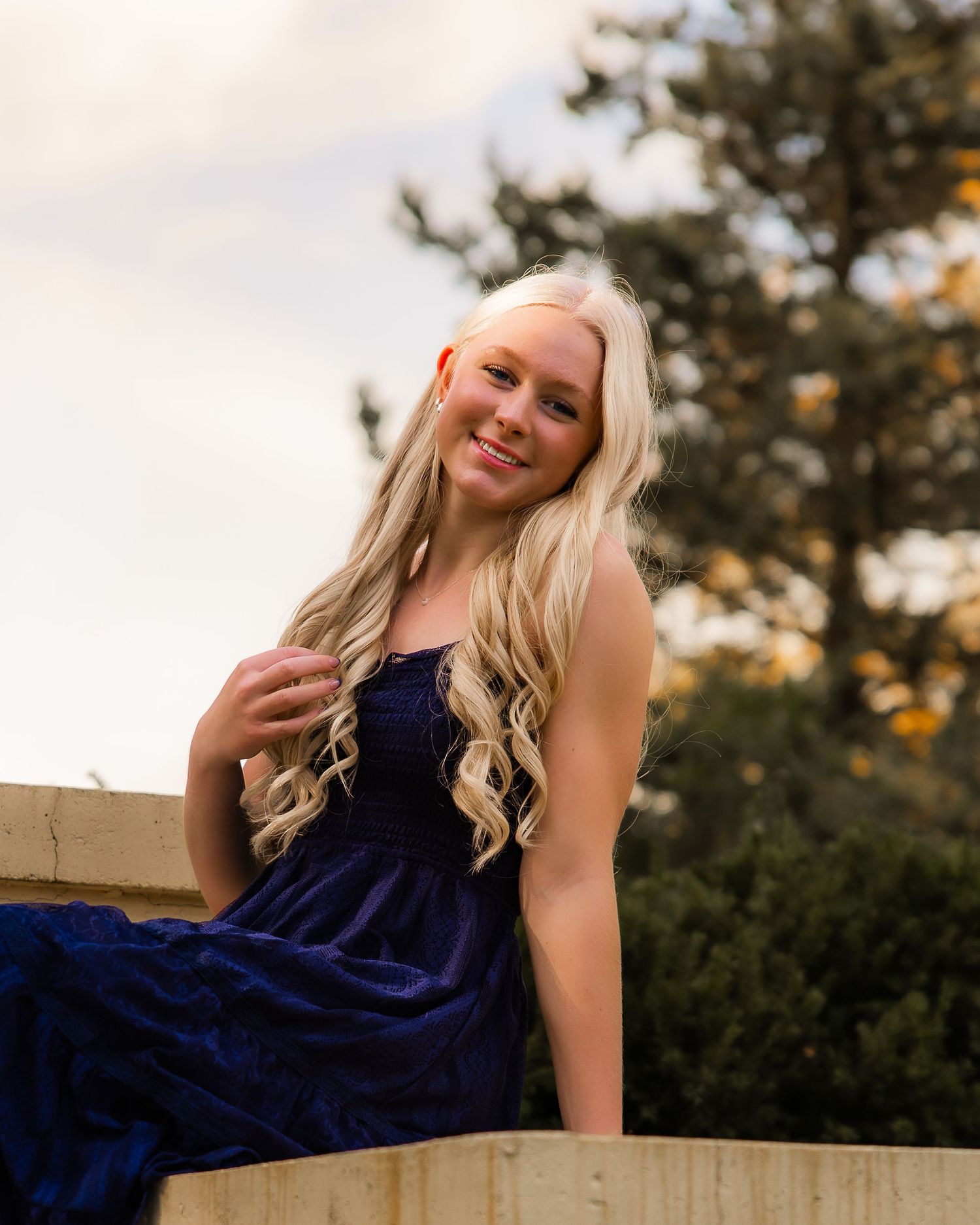 A woman in a navy blue dress poses outdoors during golden hour against a natural backdrop.