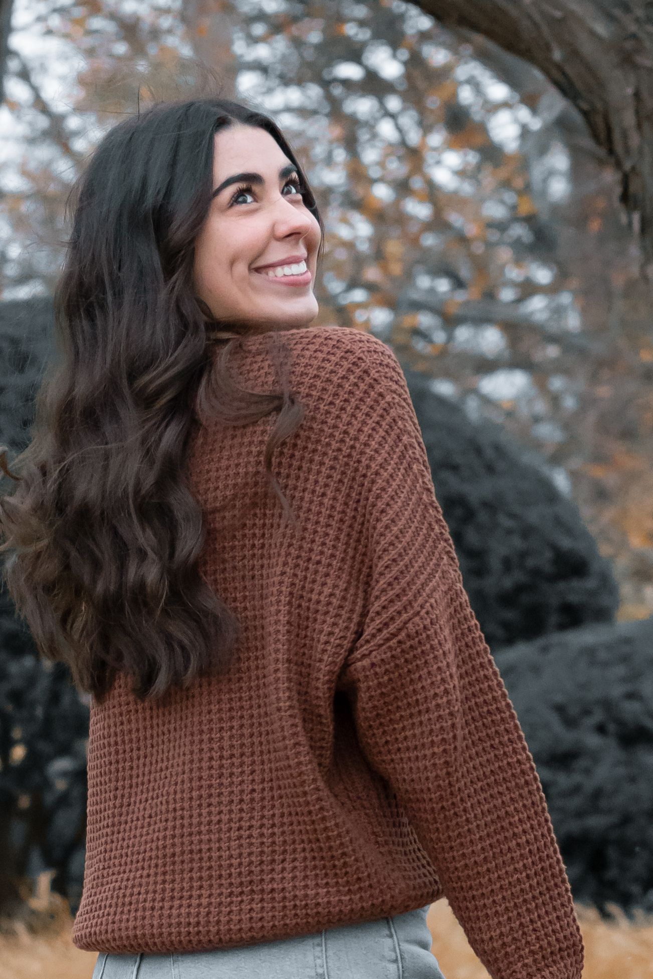 Someone wearing a brown knit sweater poses outdoors during an autumn photoshoot.