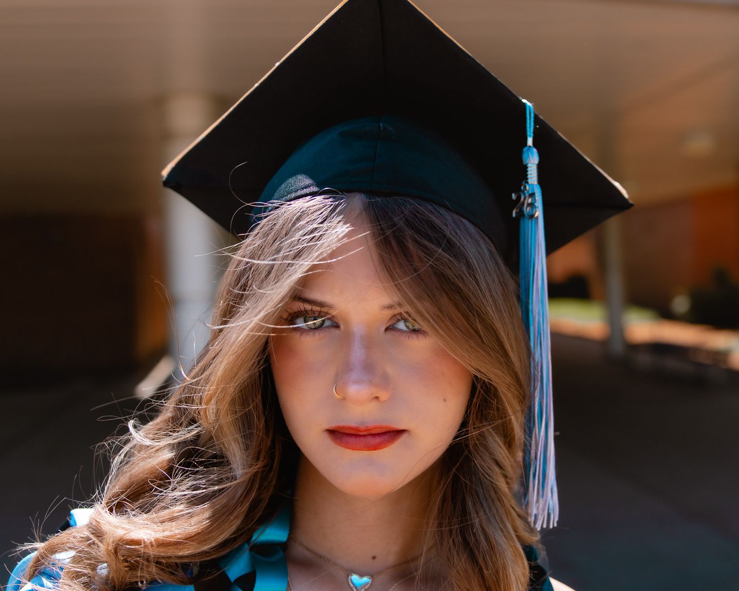 Young woman in black graduation cap and gown with teal tassel, posing outdoors for graduation photo.