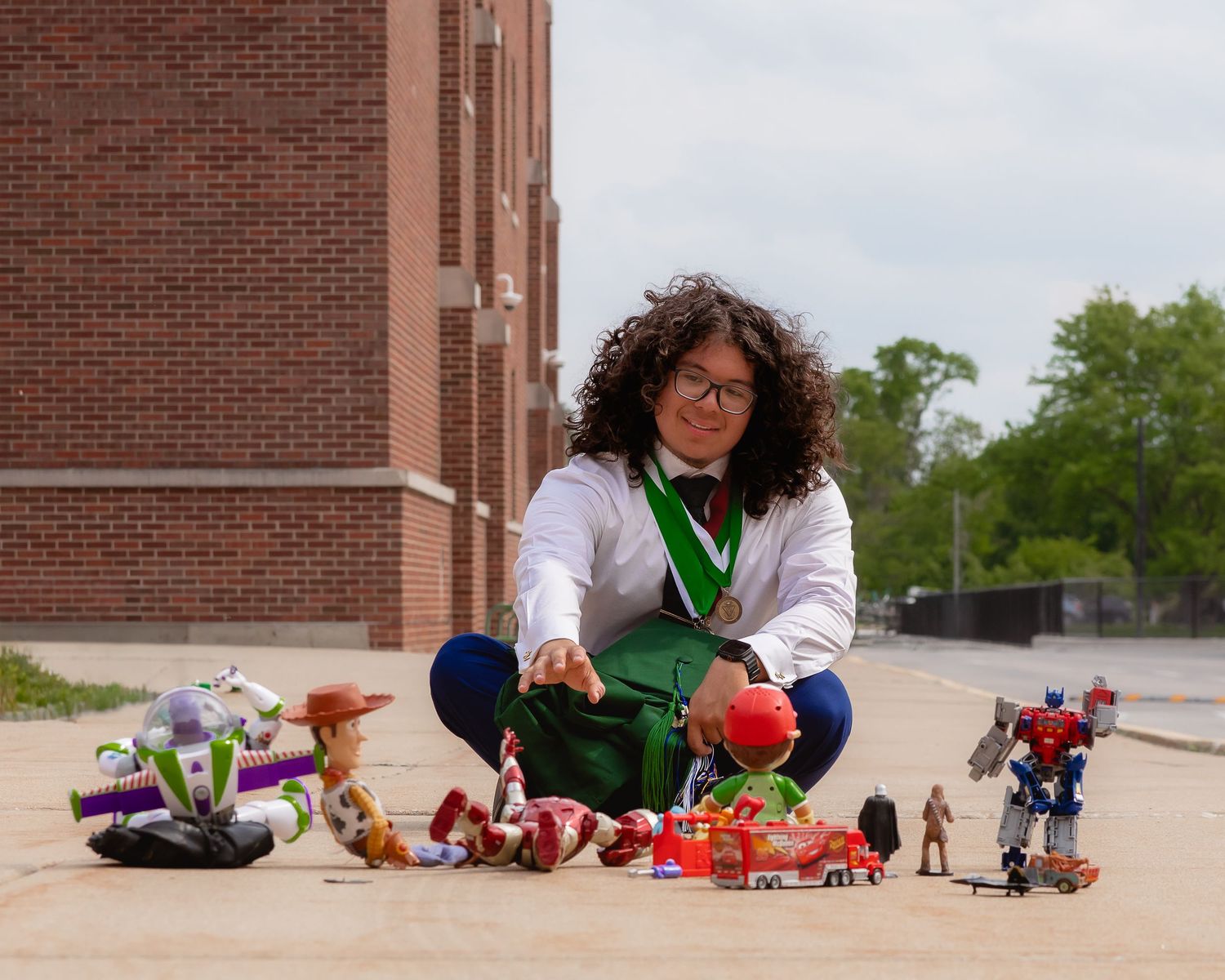 Person sitting outdoors with colorful toys including Buzz Lightyear and Transformers figures spread on the ground.