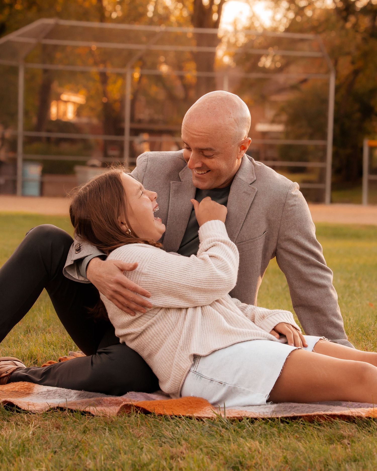 Couple shares intimate moment on picnic blanket at sunset in park.
