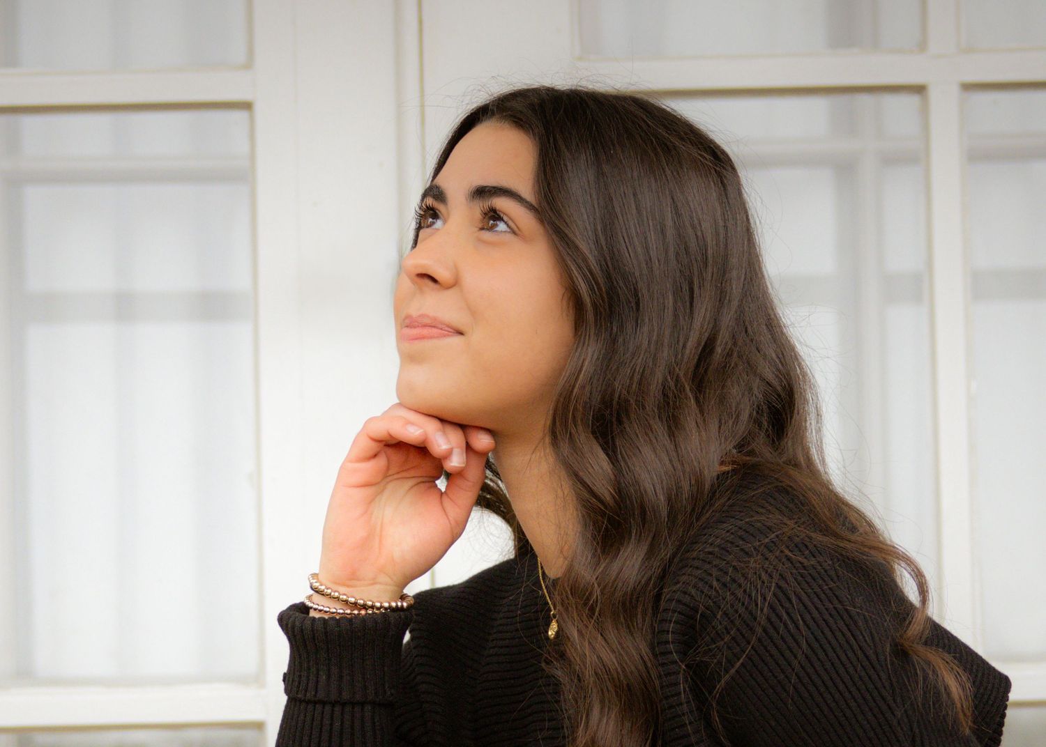 Person in black sweater sitting by window with natural light illuminating serene contemplative pose.