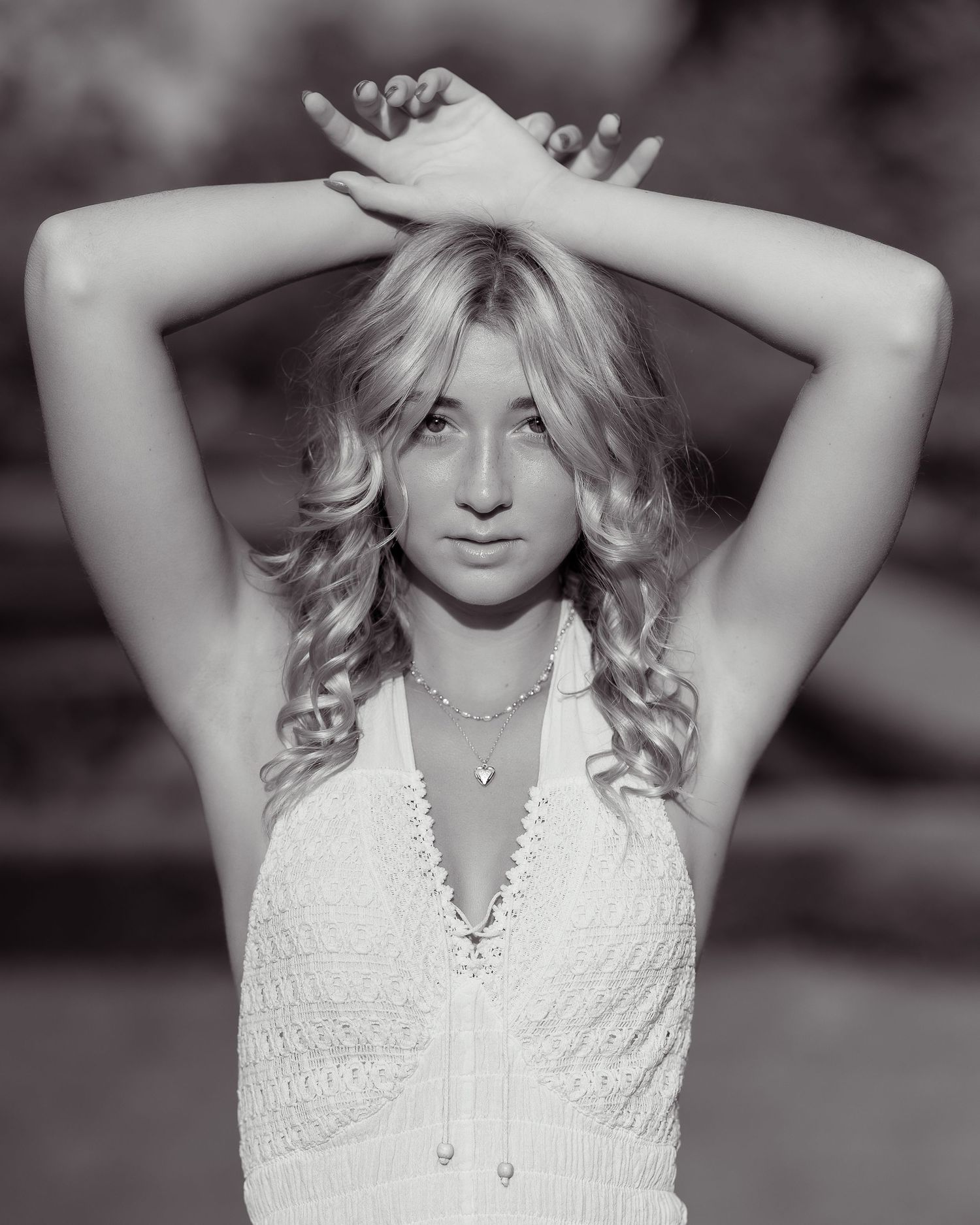 Black and white portrait of woman in lace top with arms raised above head.