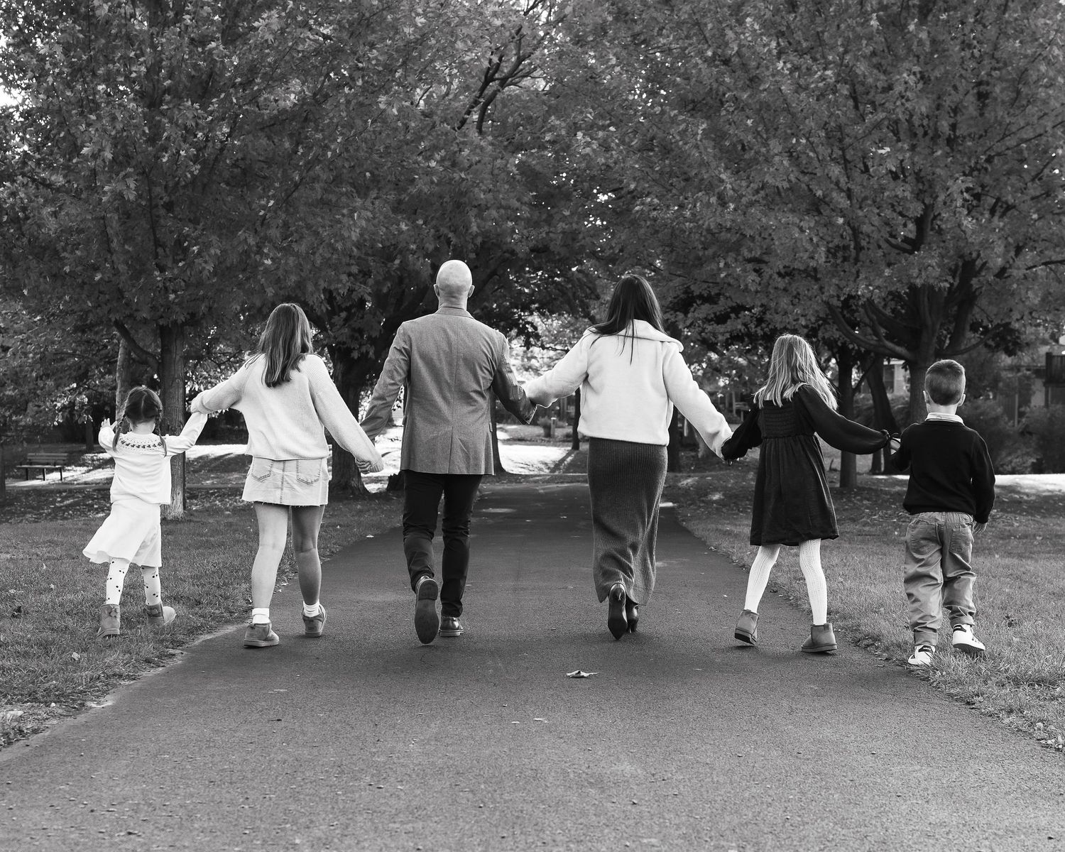 Group walks hand in hand down path in black and white photo.