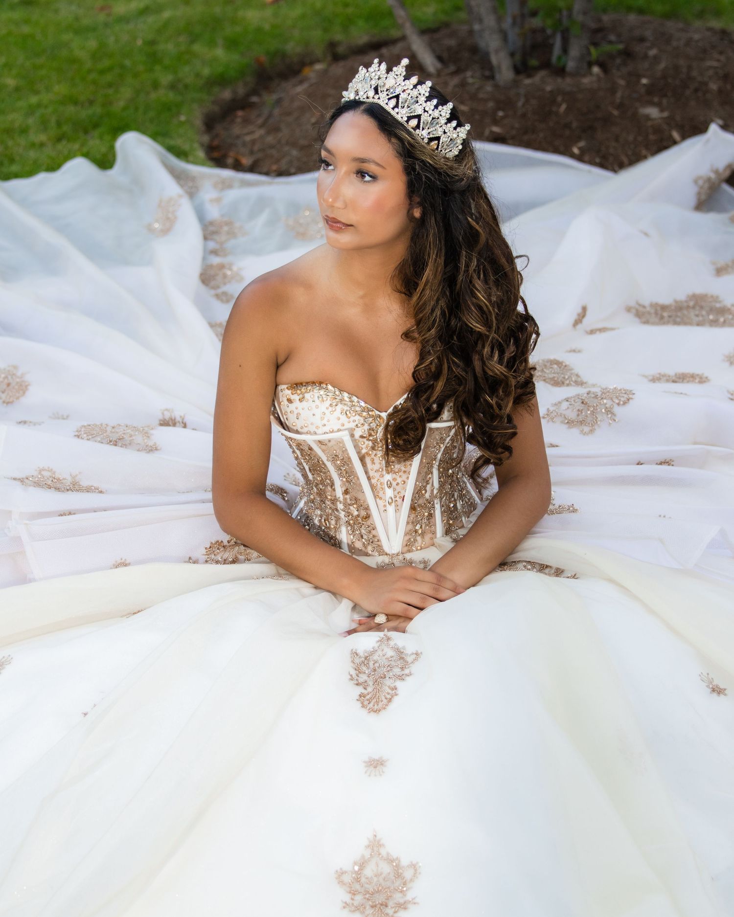 A stunning crystal-adorned tiara crowns an elegant white ball gown with a strapless corset bodice and flowing skirt.