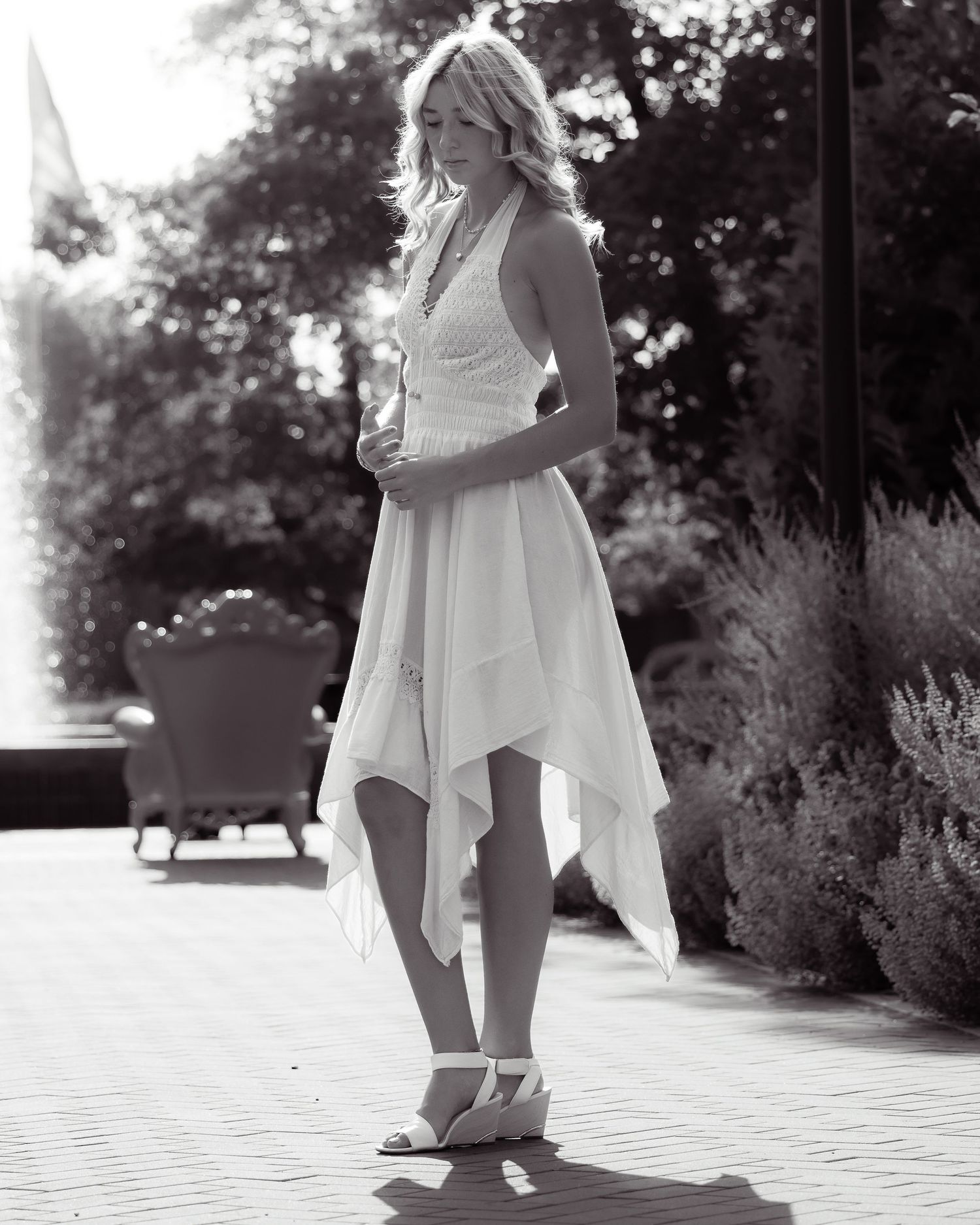Black and white fashion photo of a woman in flowing asymmetrical dress and heels on patio.