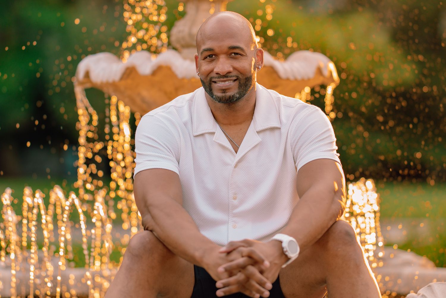 Portrait of man in white polo shirt smiling with decorative lights in background.