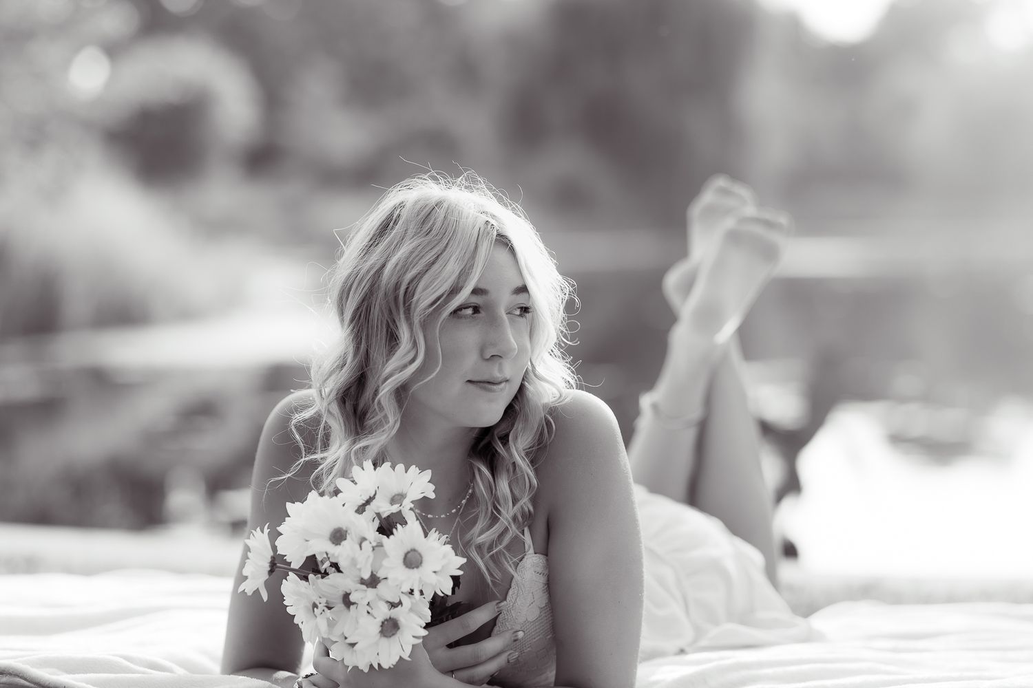 A bride in a white wedding dress lies on grass outdoors in soft natural lighting during a romantic photoshoot.