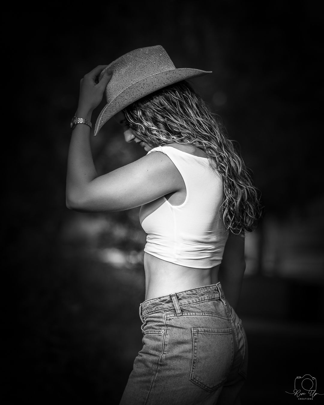 Black and white portrait of person in white top and denim with hat.