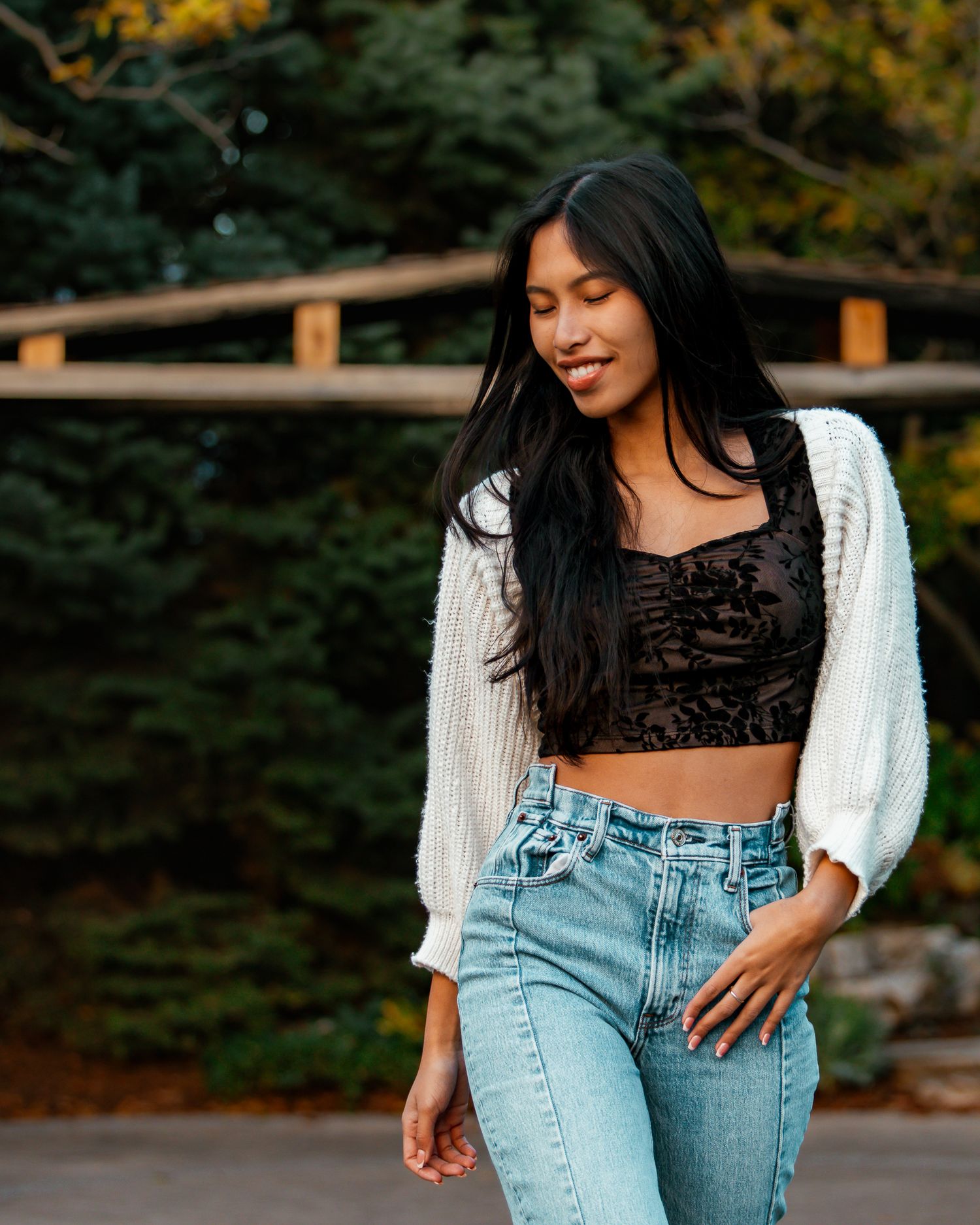 Casual fashion shoot featuring denim jeans and a white cardigan against an autumn backdrop.