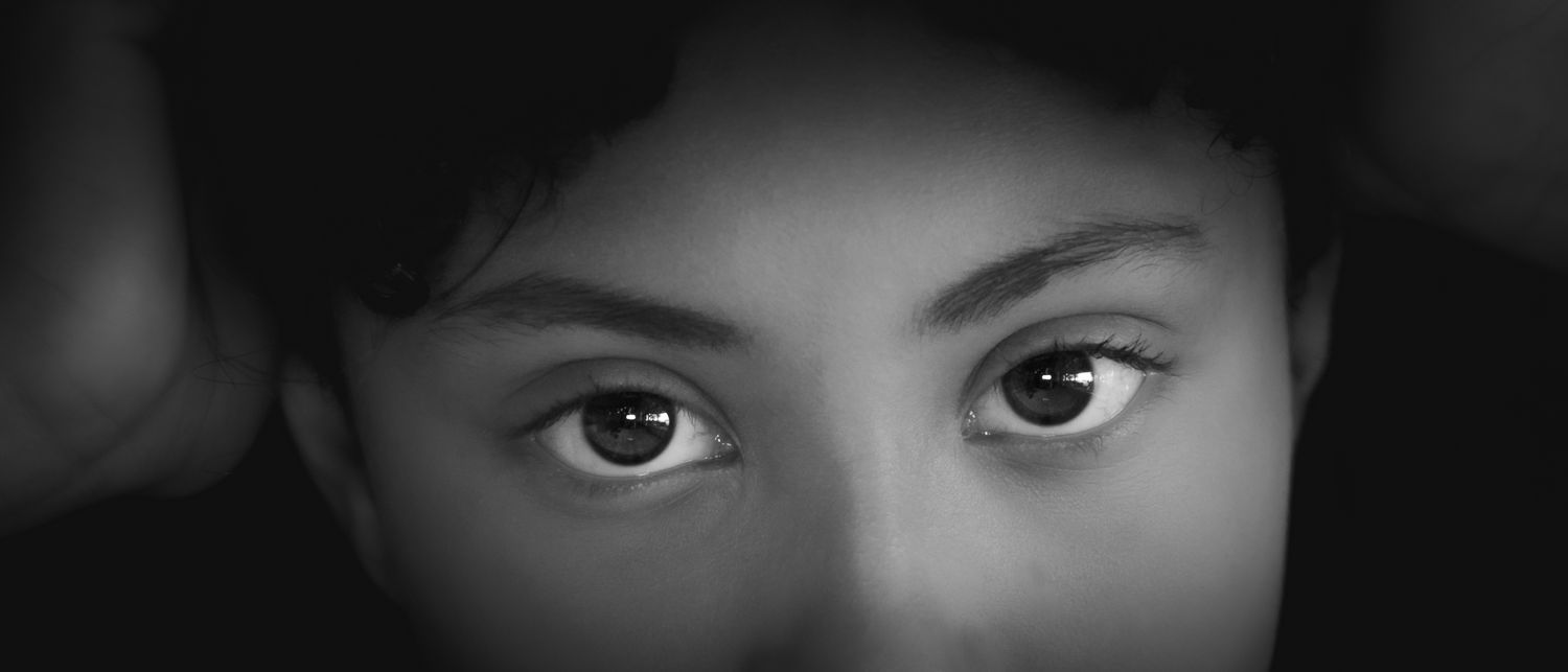 Dramatic black and white close-up portrait focusing on expressive eyes in shadow.