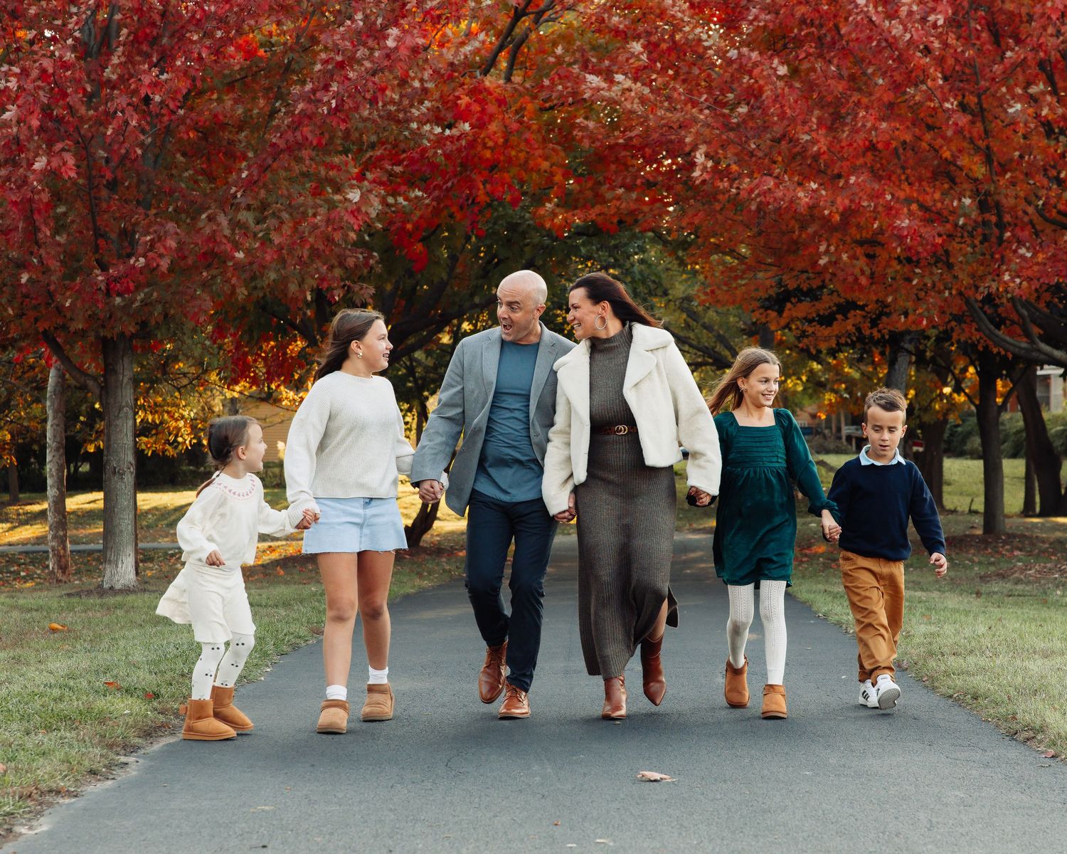 Family walks together under vibrant red autumn trees on paved path.