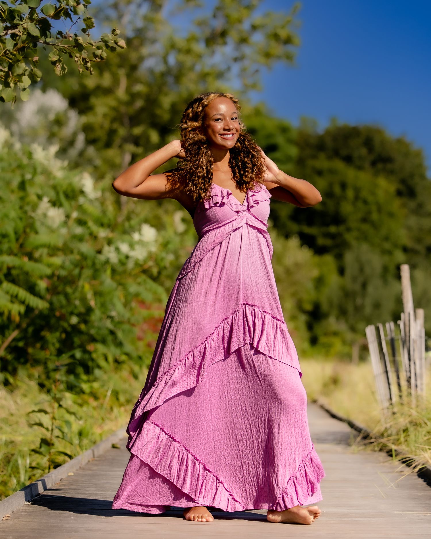 A pink summer dress moves playfully along a wooden boardwalk path surrounded by greenery.