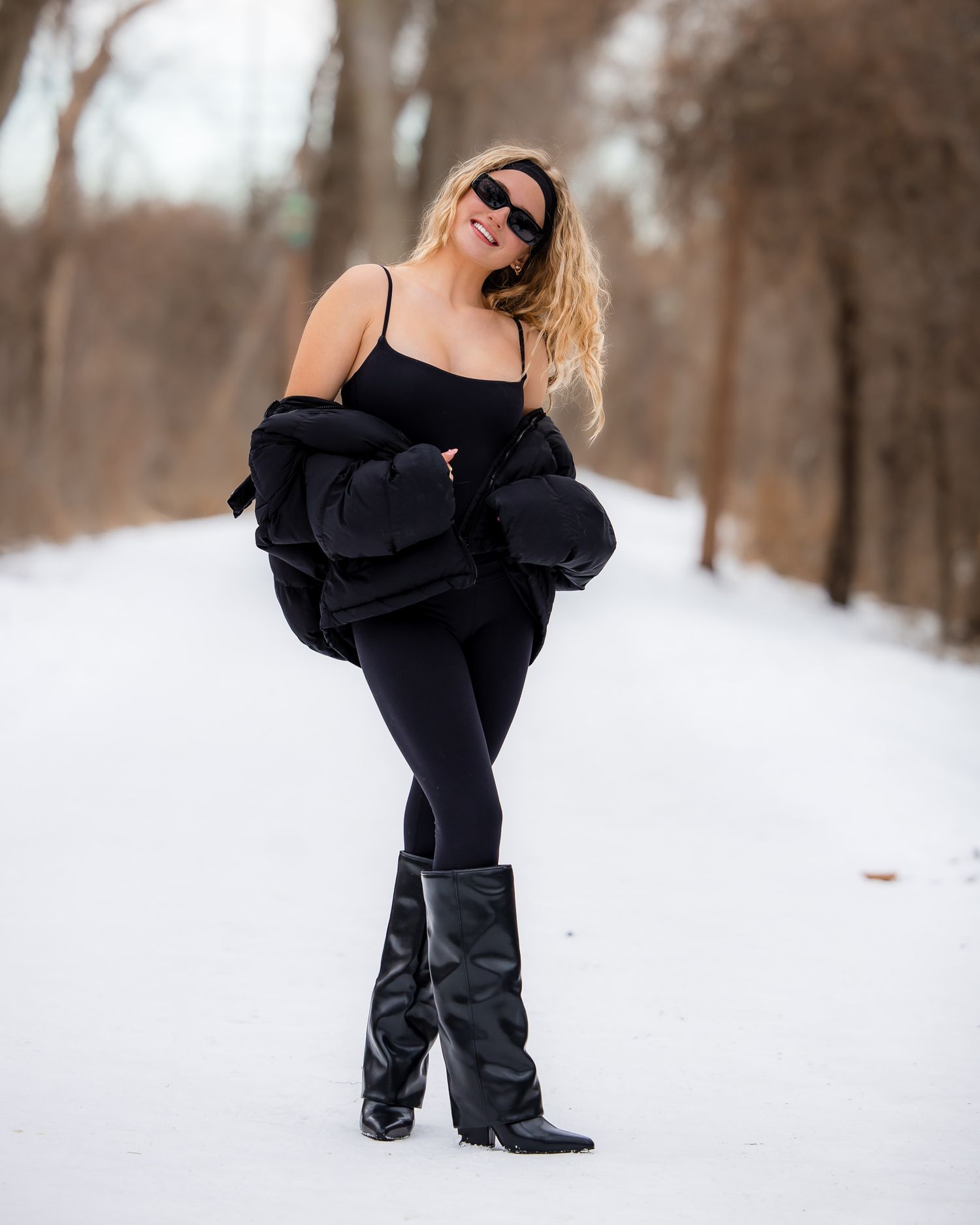 A person in a black outfit poses playfully in the snow during a winter photoshoot.