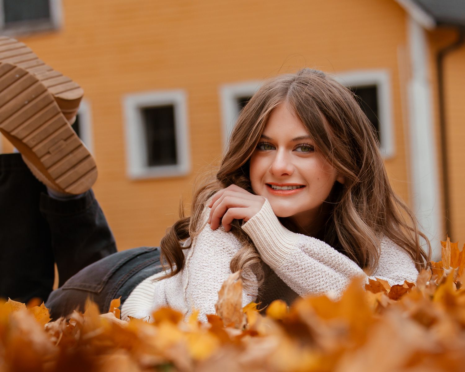 A person wearing a cream knit sweater plays in fallen autumn leaves on a sunny fall day.