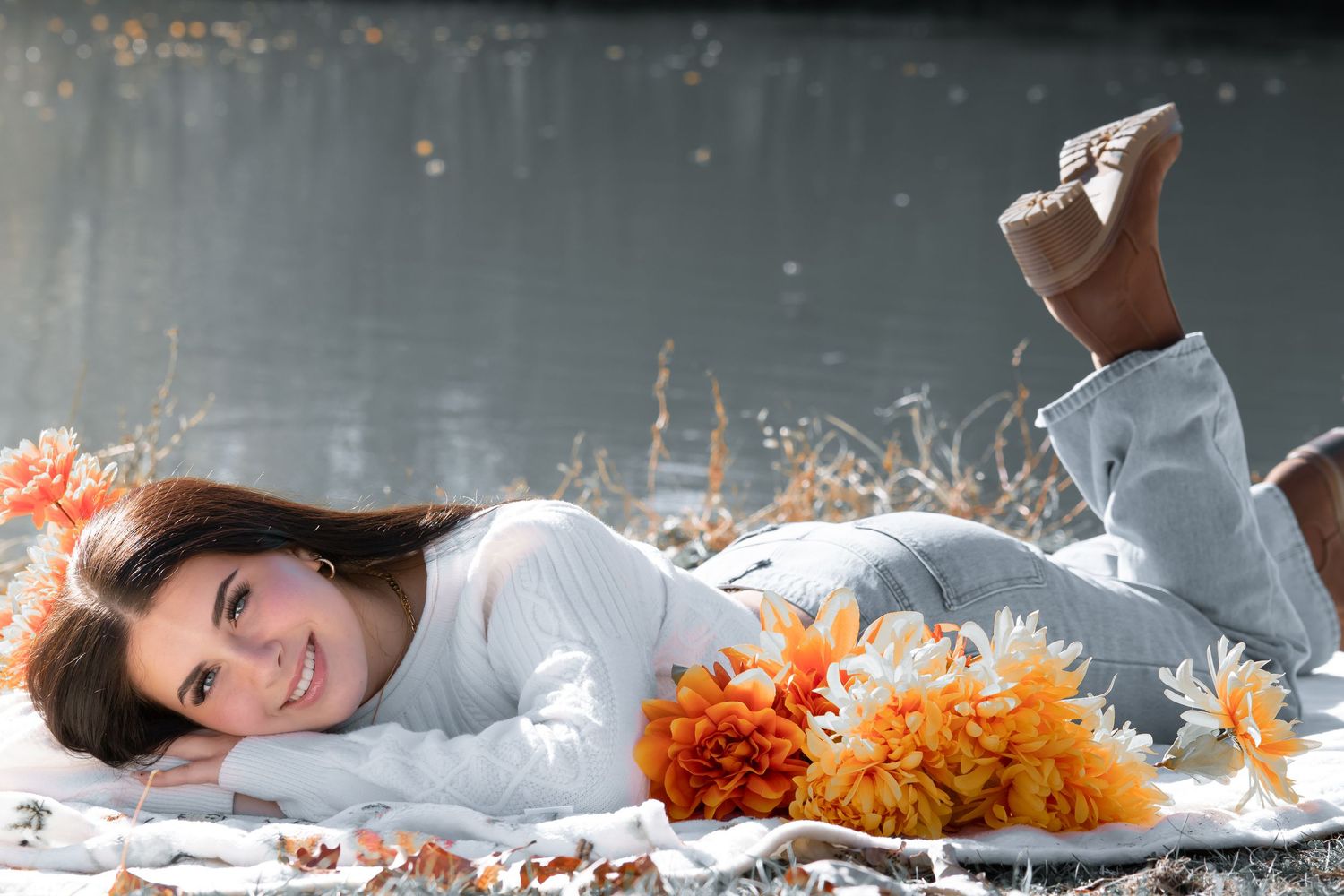 Lifestyle portrait on blanket with orange flowers and white sweater in relaxed pose.