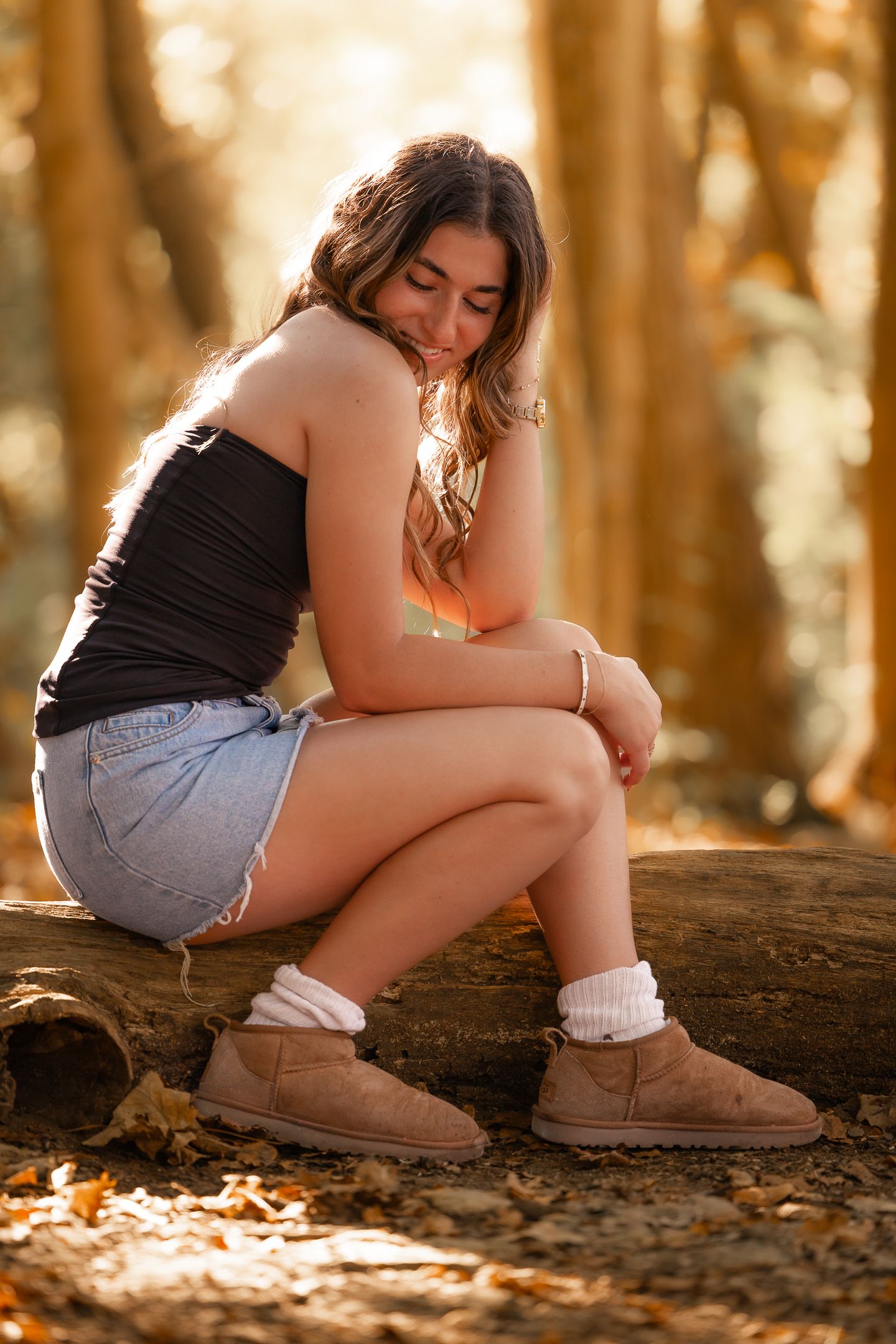 Woman in casual attire sitting on log in sunlit forest wearing boots and denim shorts.