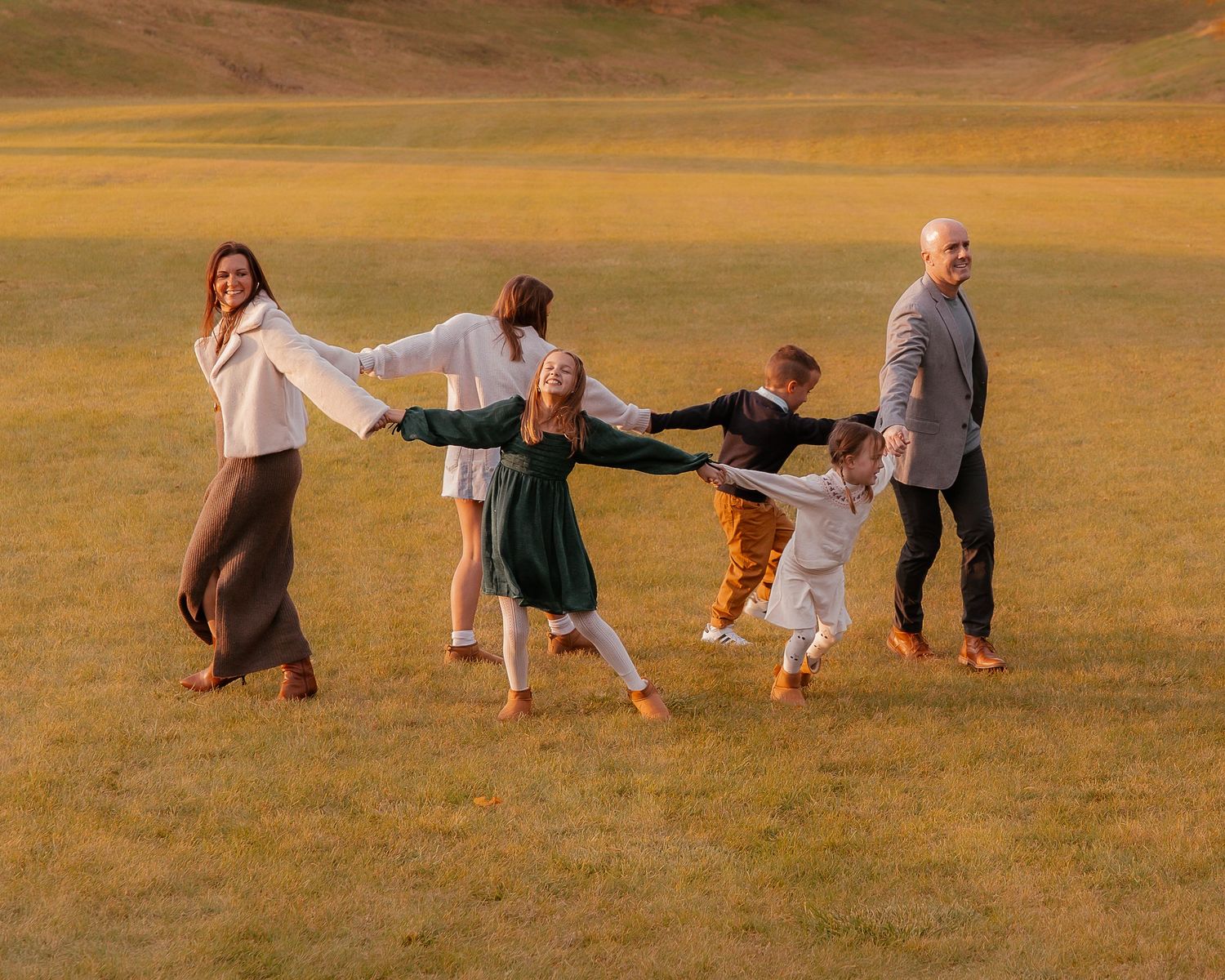 Family plays and runs together in open field during sunset.