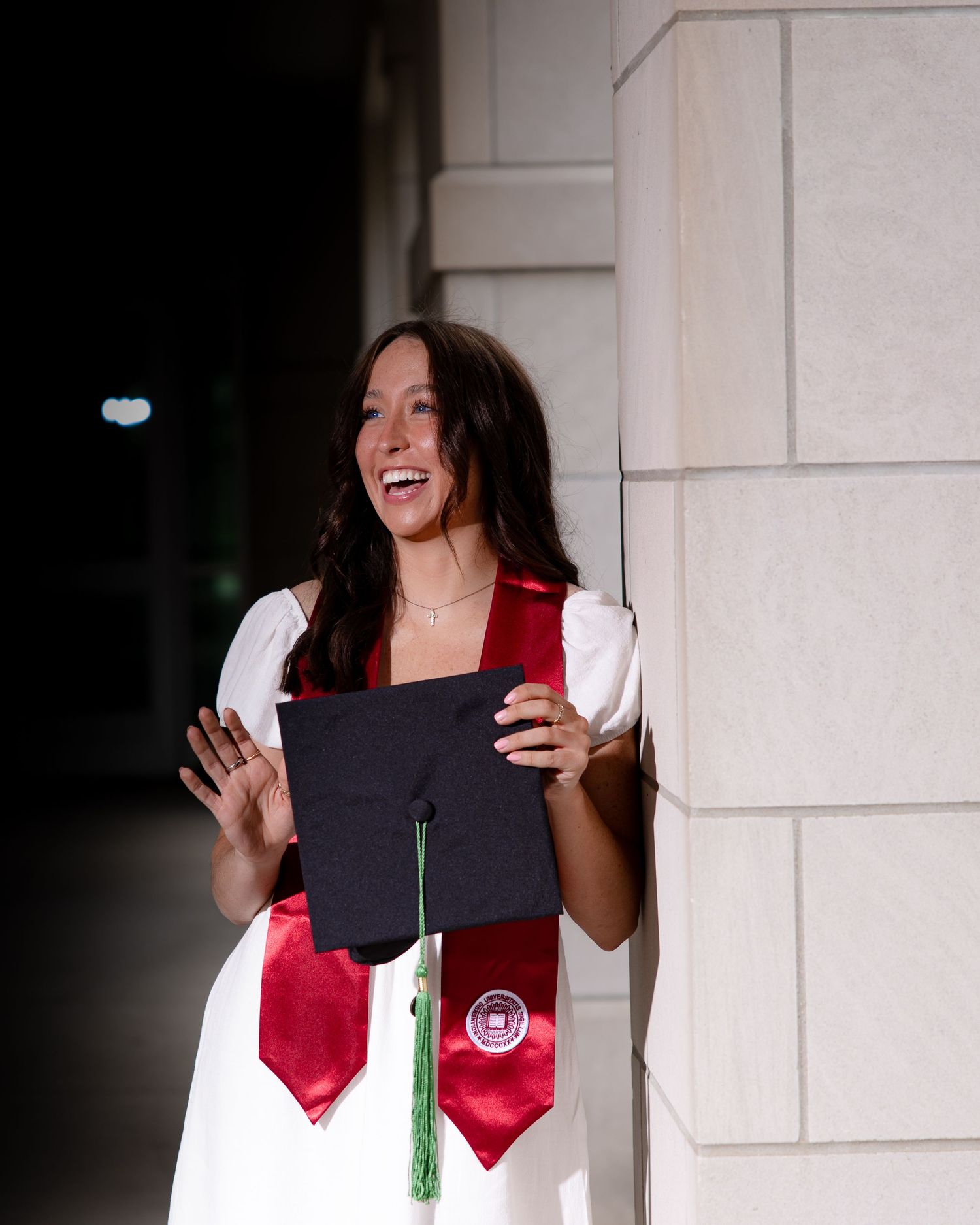 Graduate celebrating with diploma and stole in dramatic lighting.