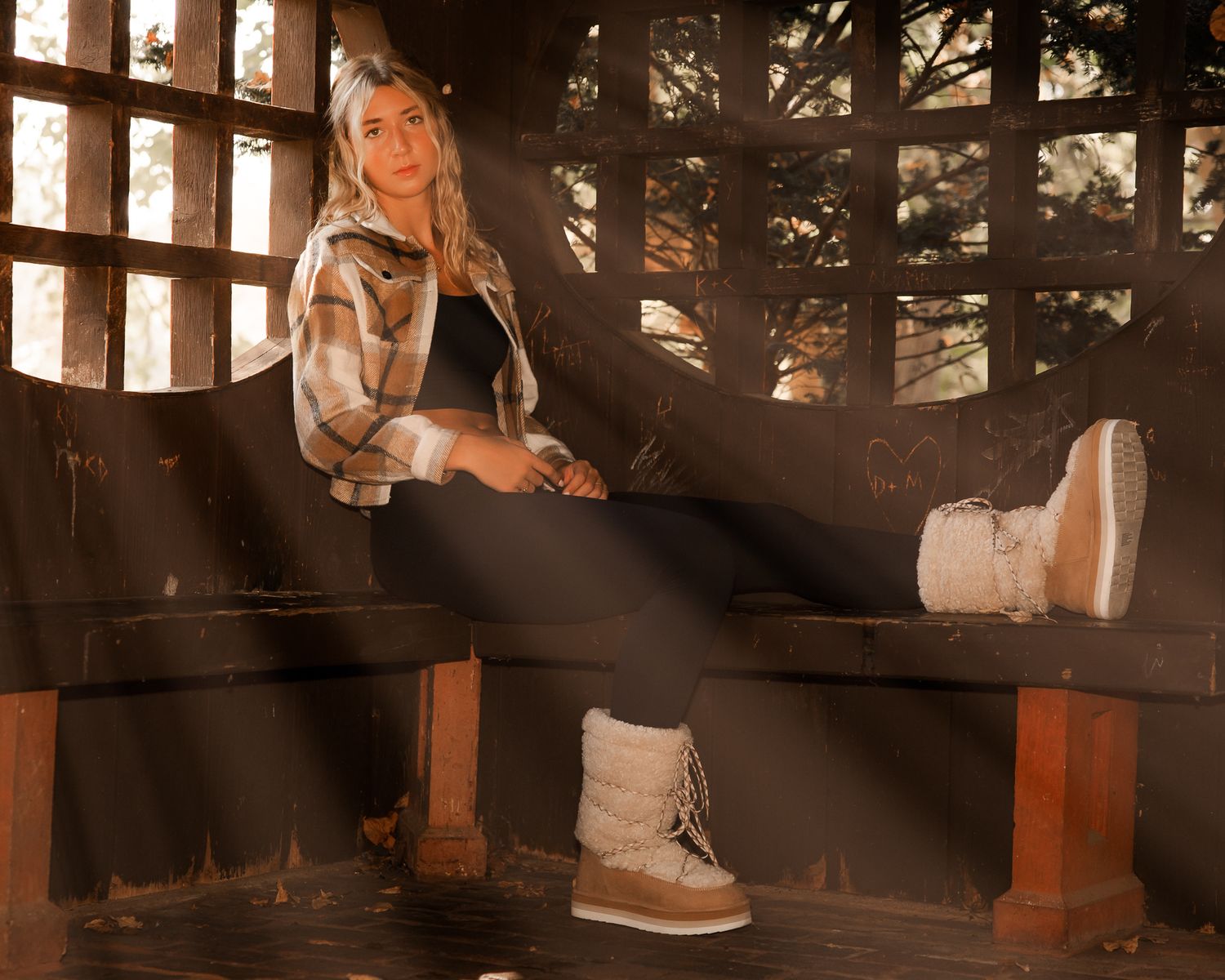 Person relaxing on wooden bench with sunlight streaming through slats creating dramatic shadows.
