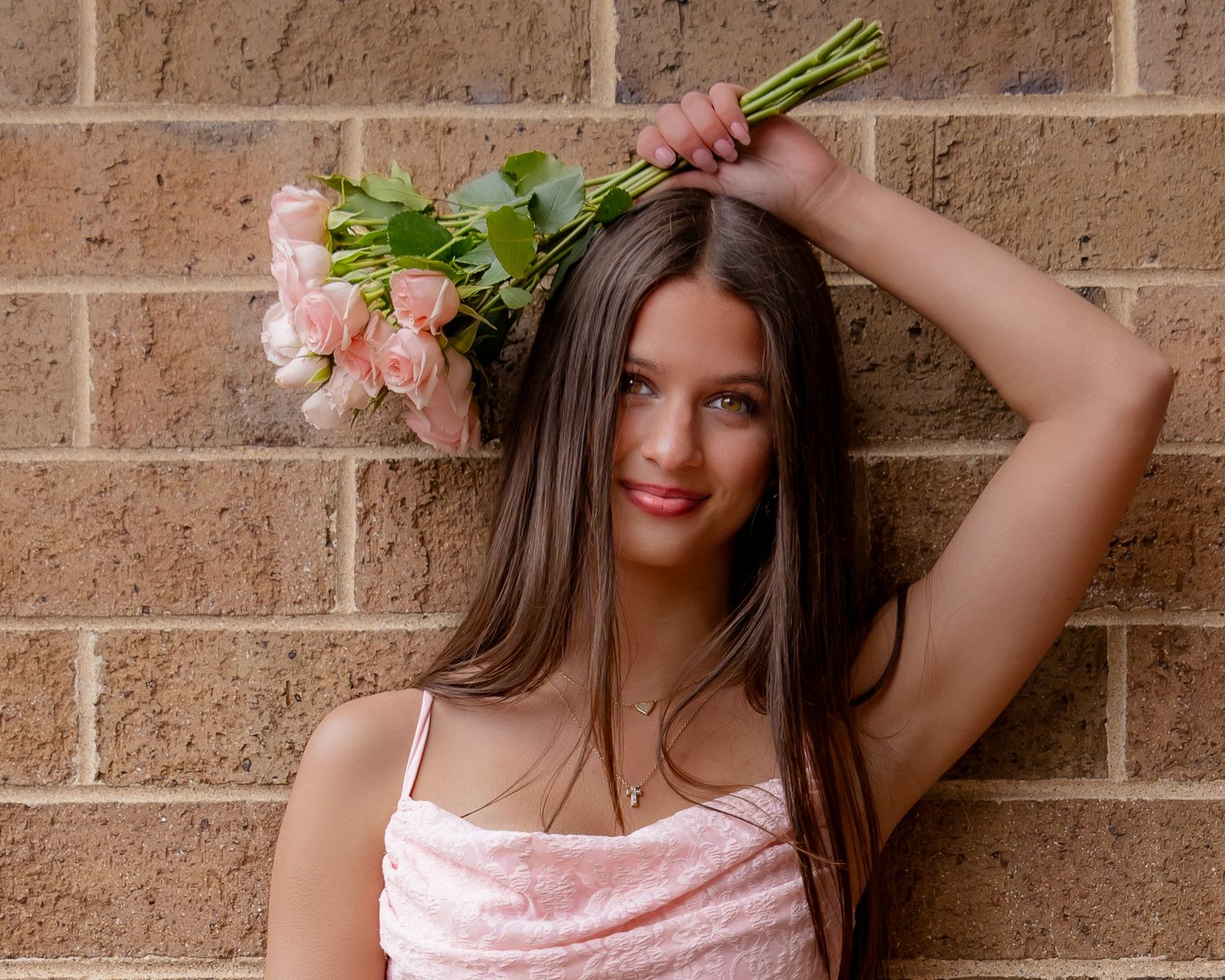 A person in a pink dress poses against a brick wall while holding fresh green celery stalks.