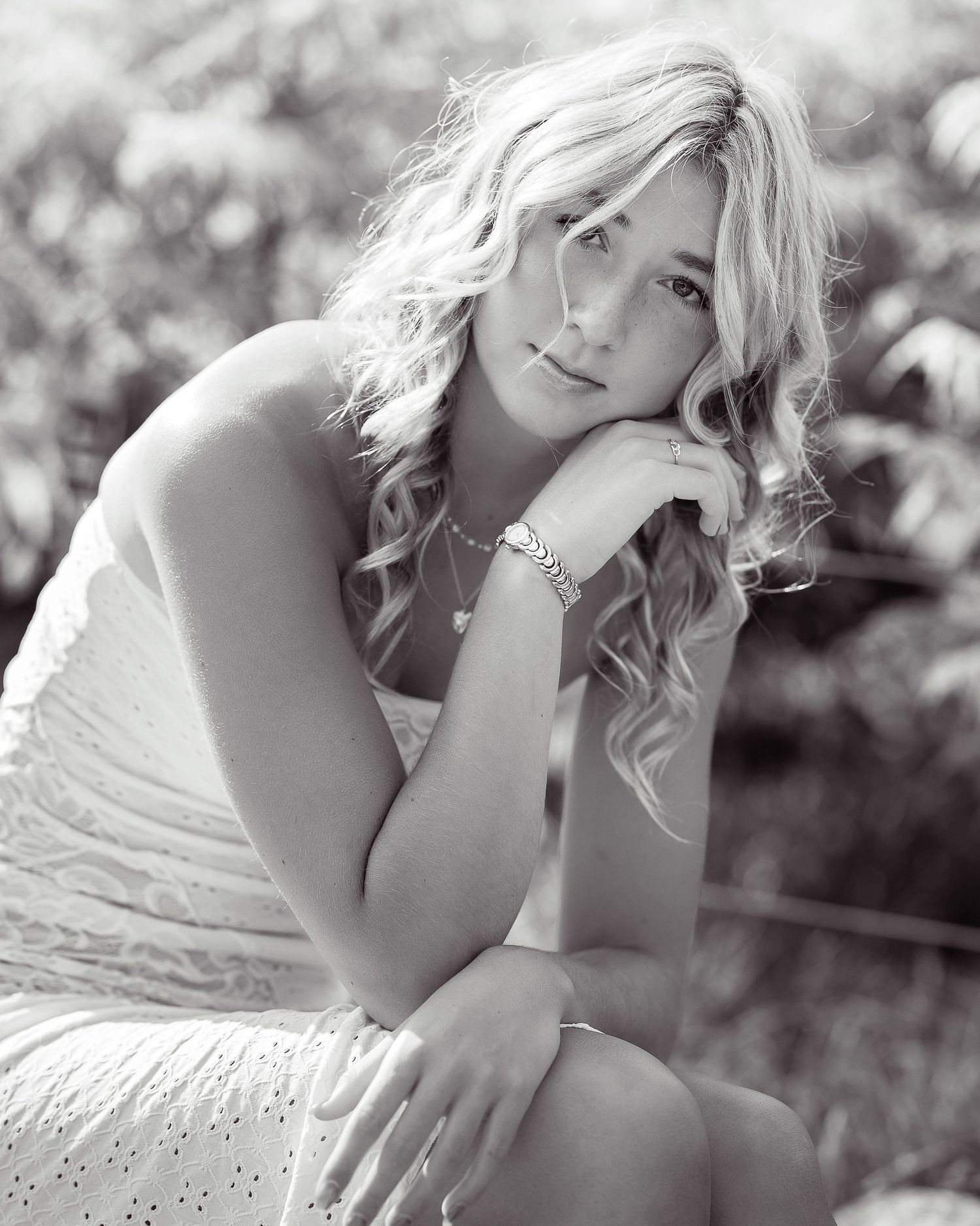 Black and white portrait of a woman in white dress posing thoughtfully outdoors.