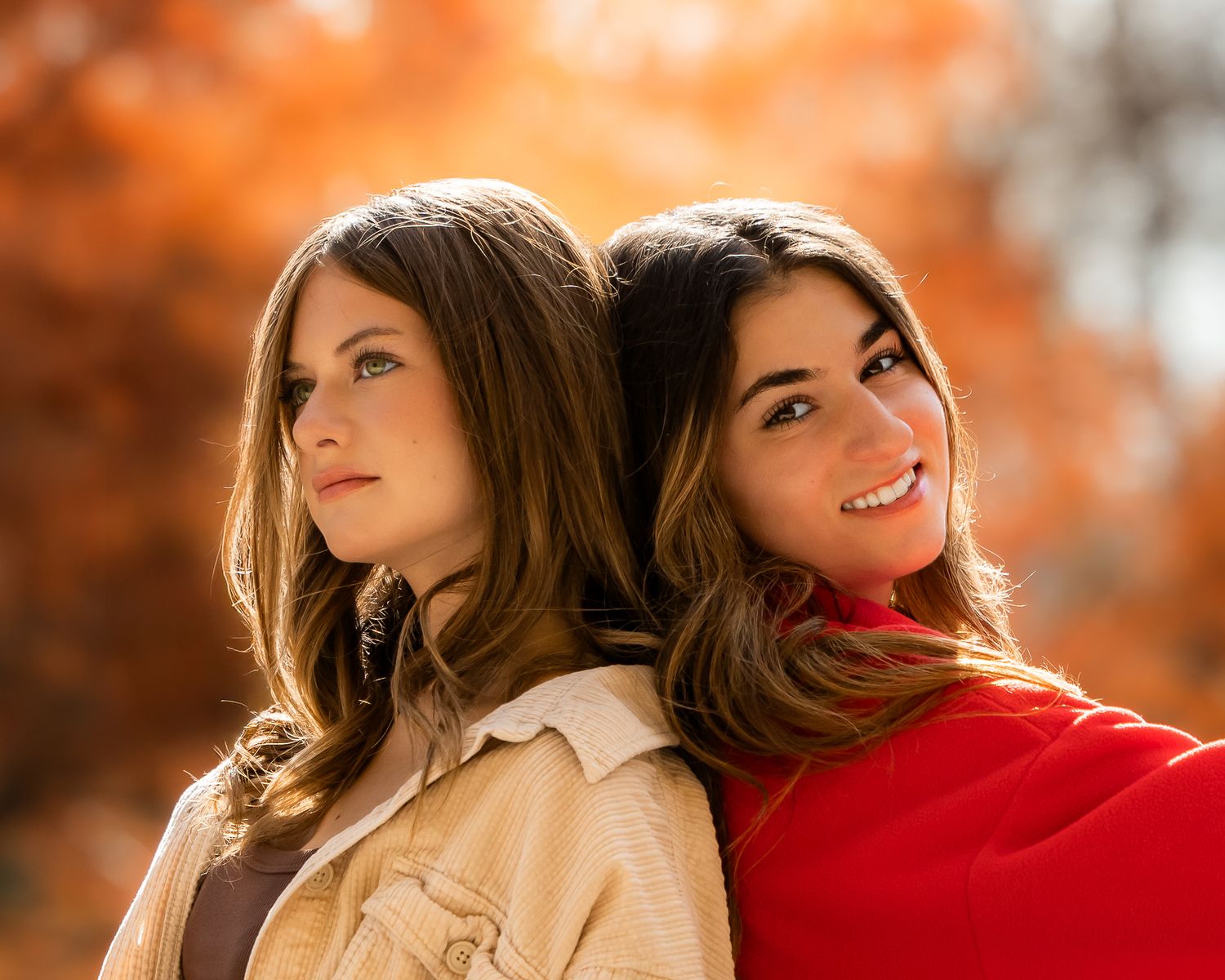 Autumn fashion portrait featuring red and beige coats against vibrant orange fall colors.