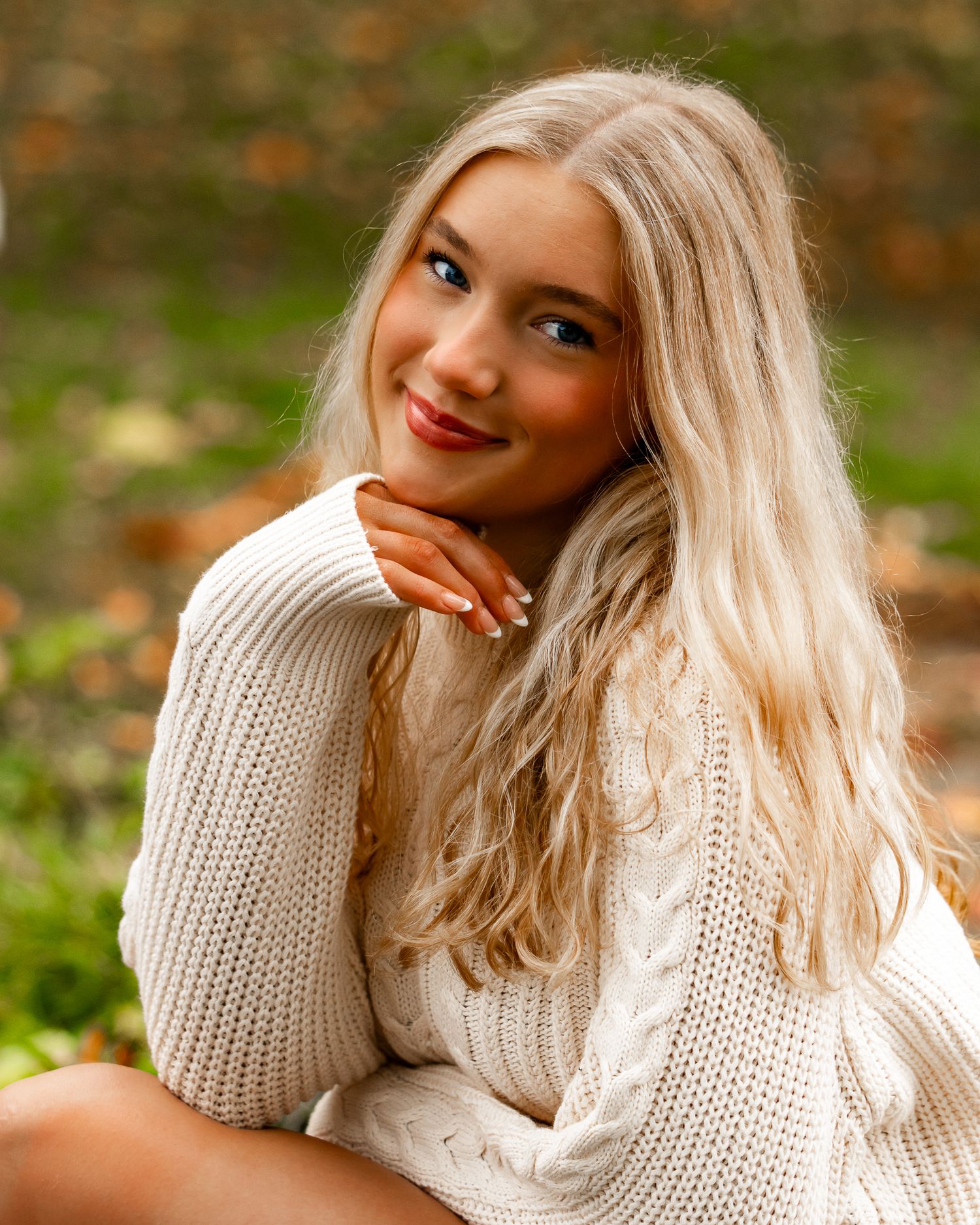 Woman in cozy white knit sweater posing outdoors during fall season.