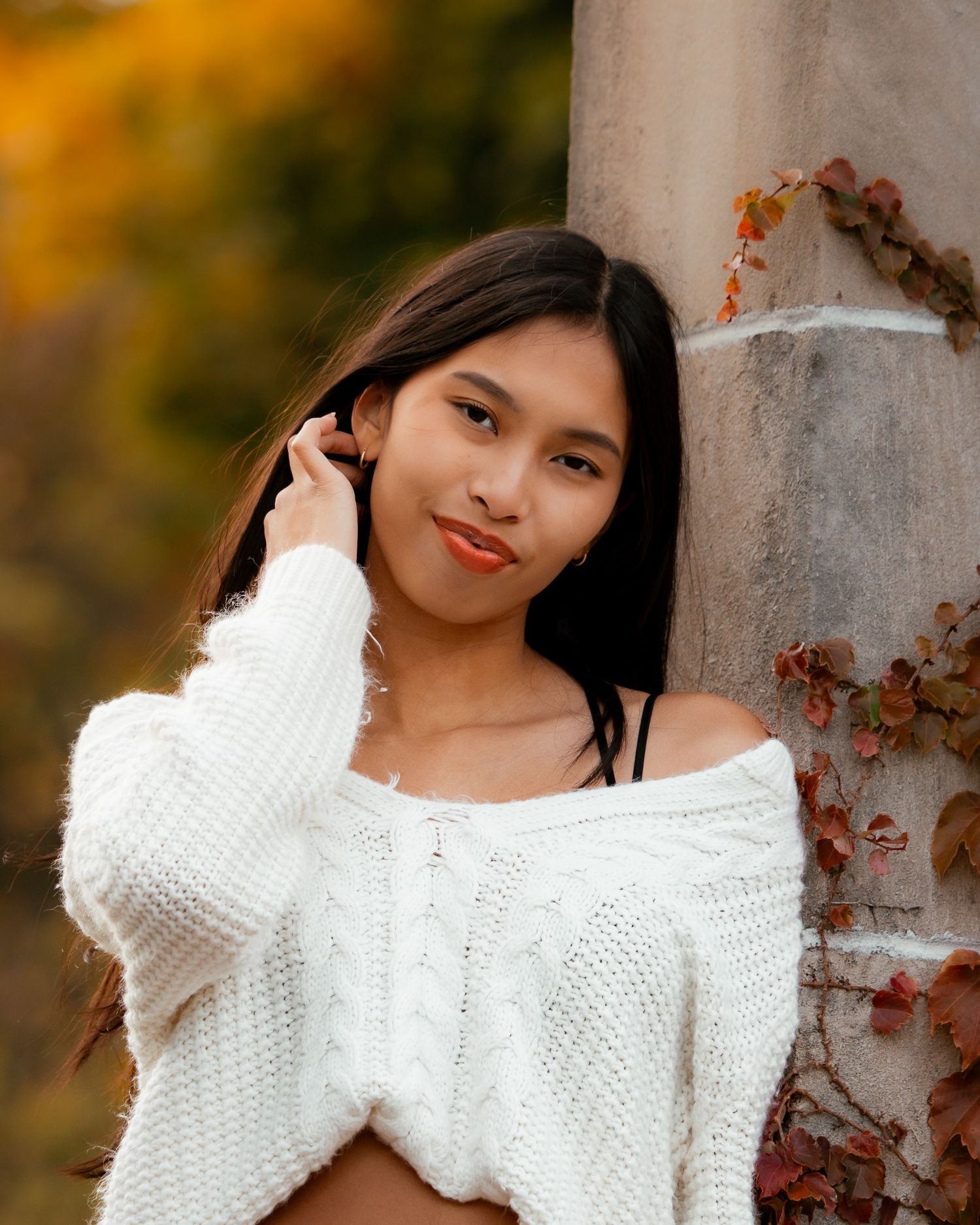 Someone in a white cable knit sweater poses against an autumn background.