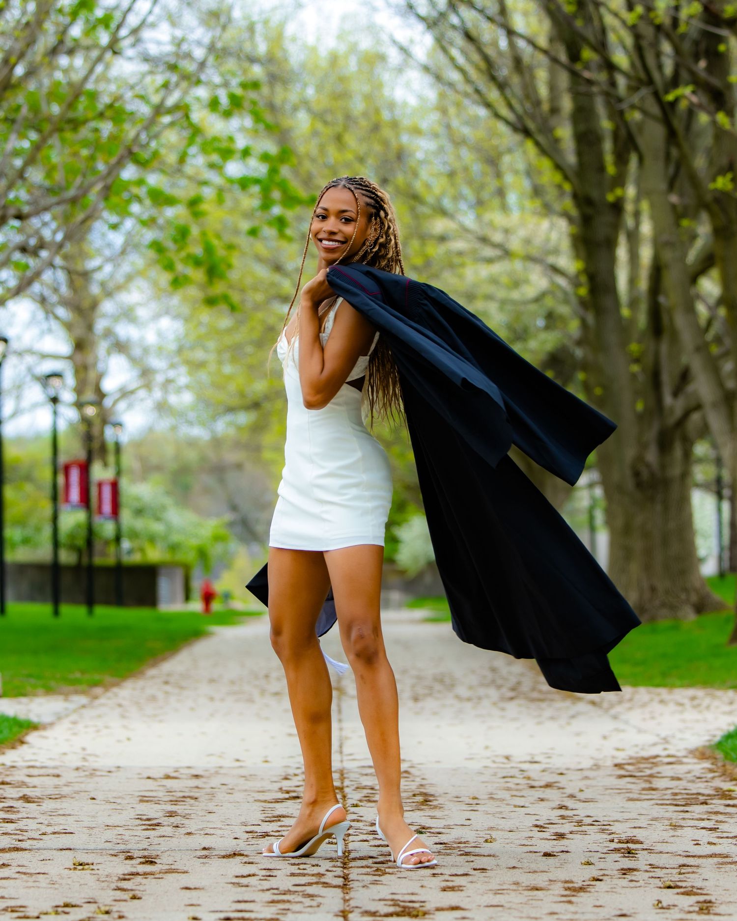 Person in white dress and black jacket twirling playfully on outdoor path.