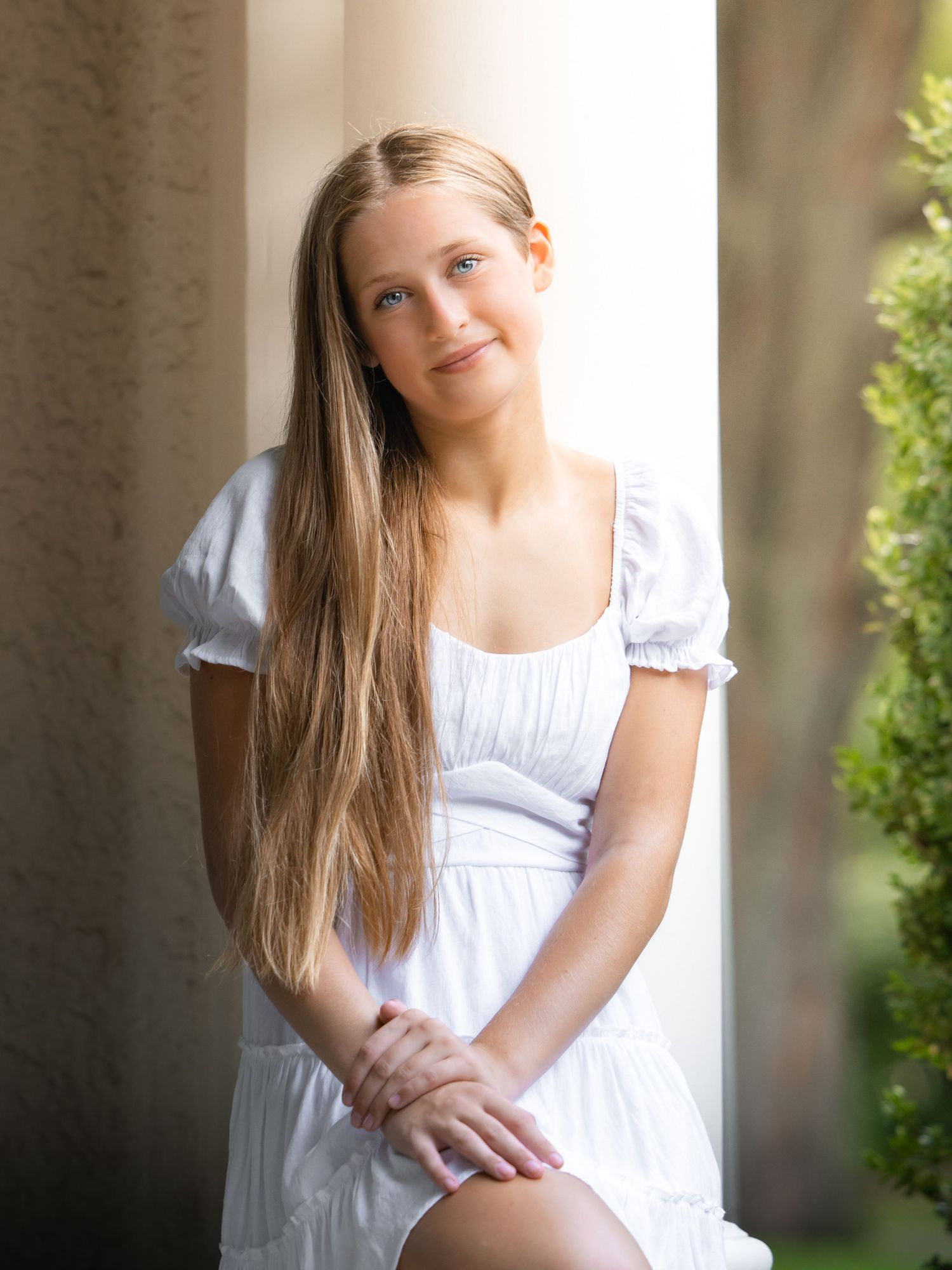 Portrait session in white dress against stone columns with natural lighting.