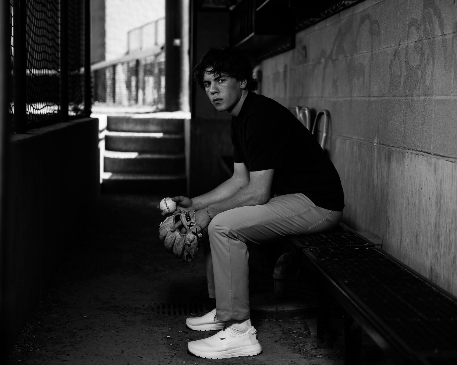 Black and white photo of a person sitting on bench in dark urban setting wearing casual clothes.