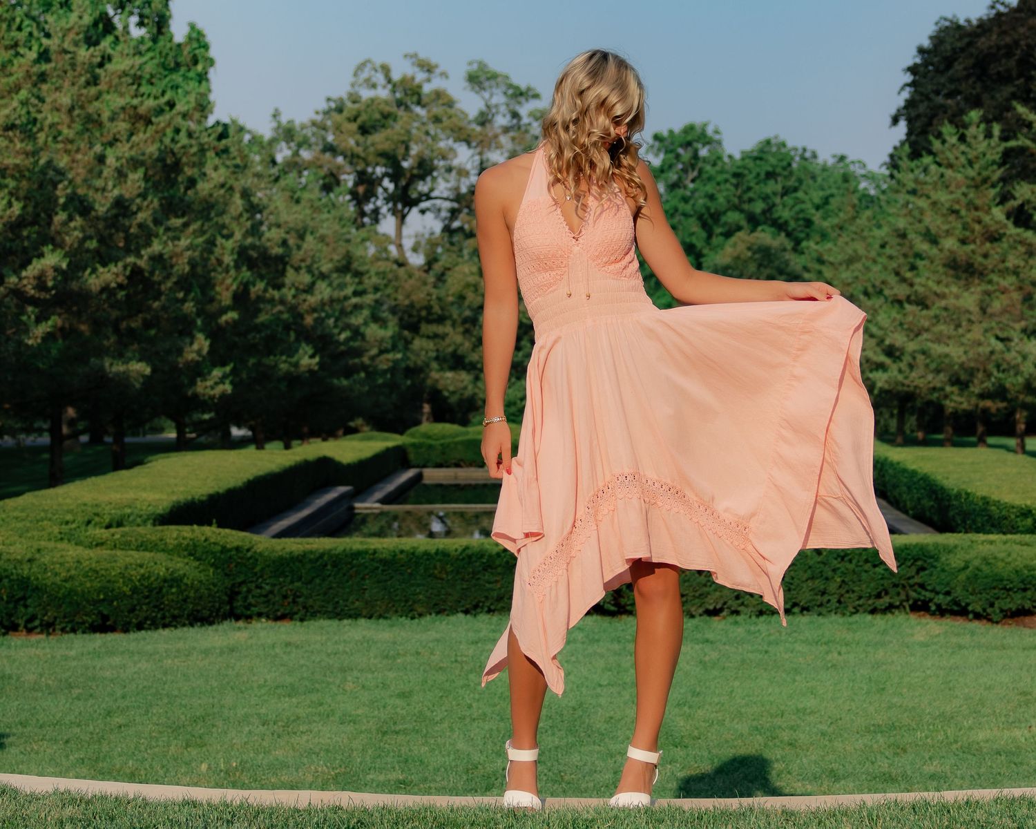 A flowing peach-colored dress billows gracefully in the breeze against a lush green garden landscape.